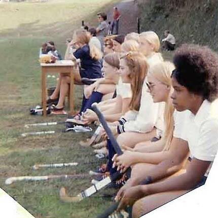 Vintage photo of field hockey players with their equipment, sitting on a bench in the grass