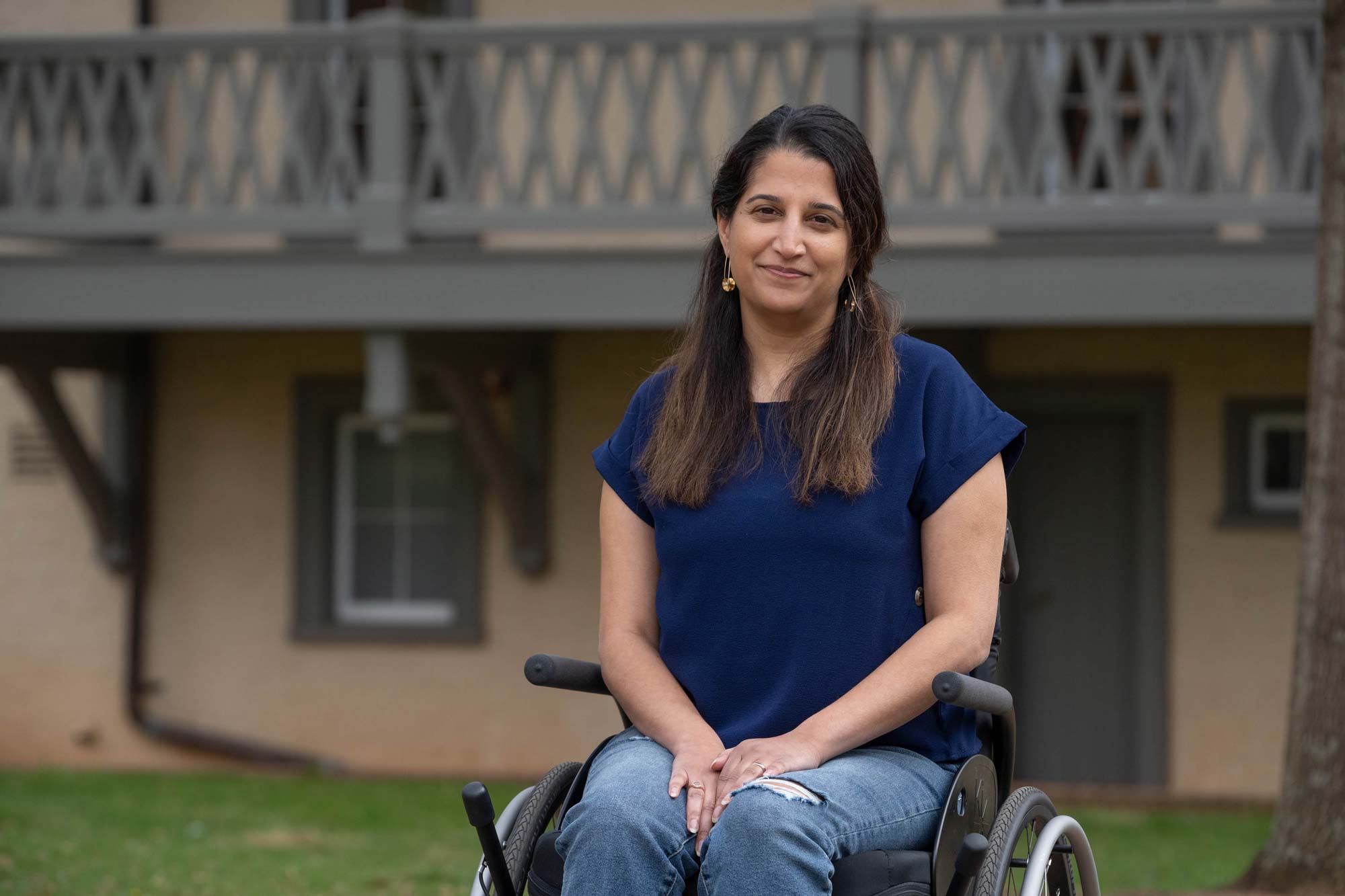 Rupa Valdez in a blue shirt and jeans sits in a wheelchair smiling