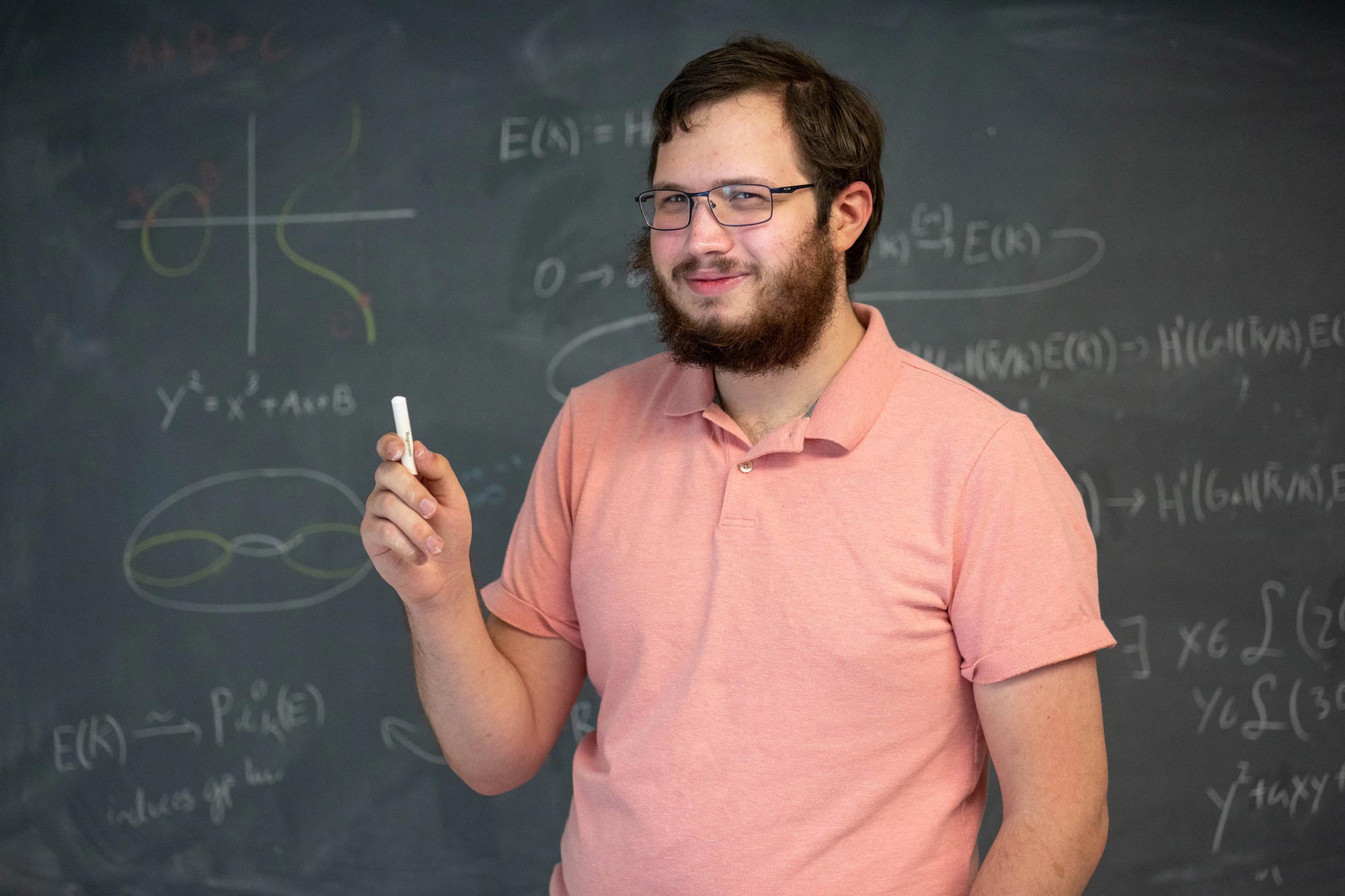 Spencer Martin, in front of a blackboard, holds a piece of chalk and smiles