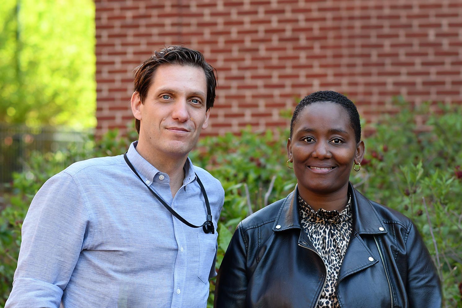 Scott Heysell and Stellah Mpagama pose for a portrait in front of a brick building