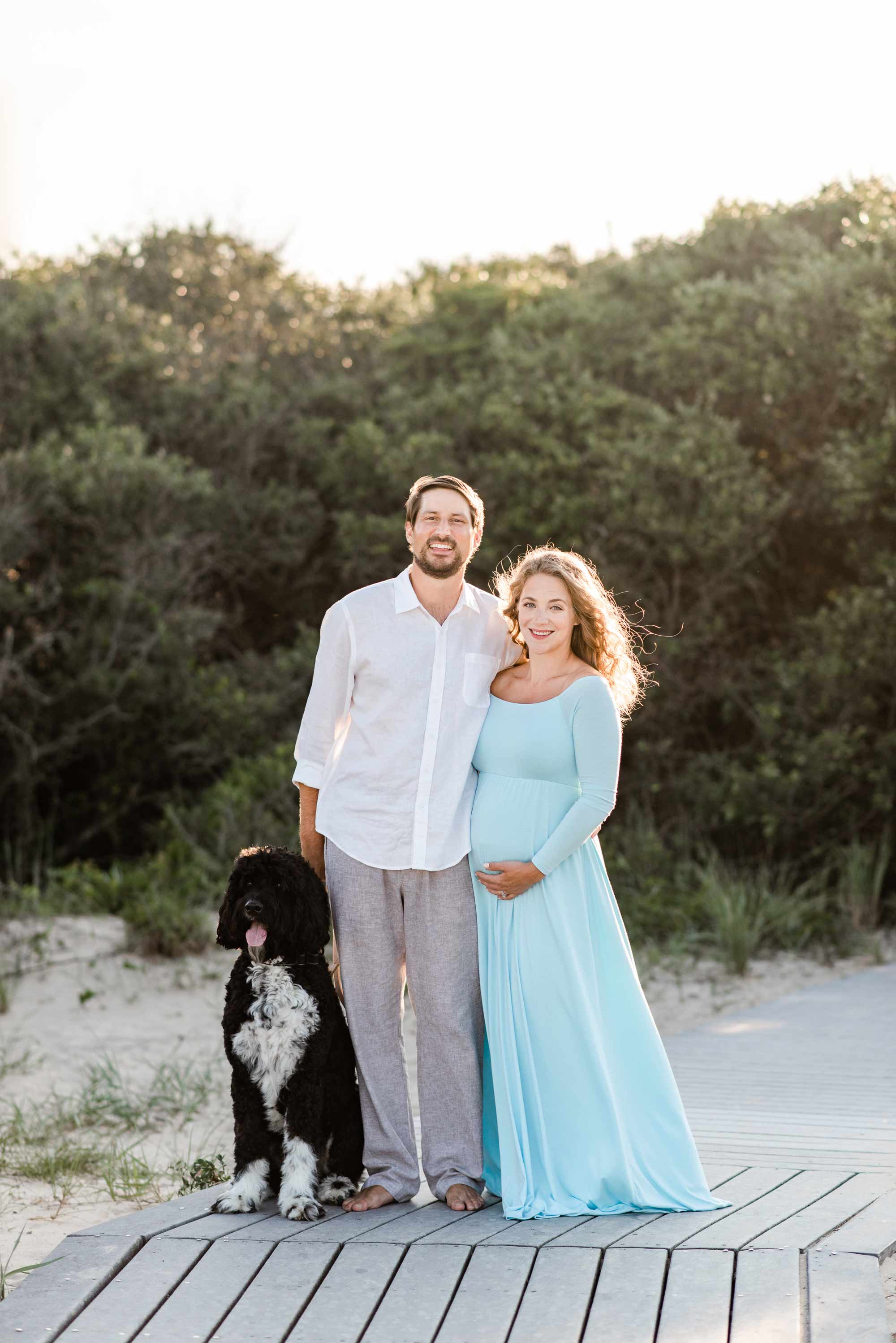 A pregnant Kelsey Summer poses for a portrait with her husband and dog