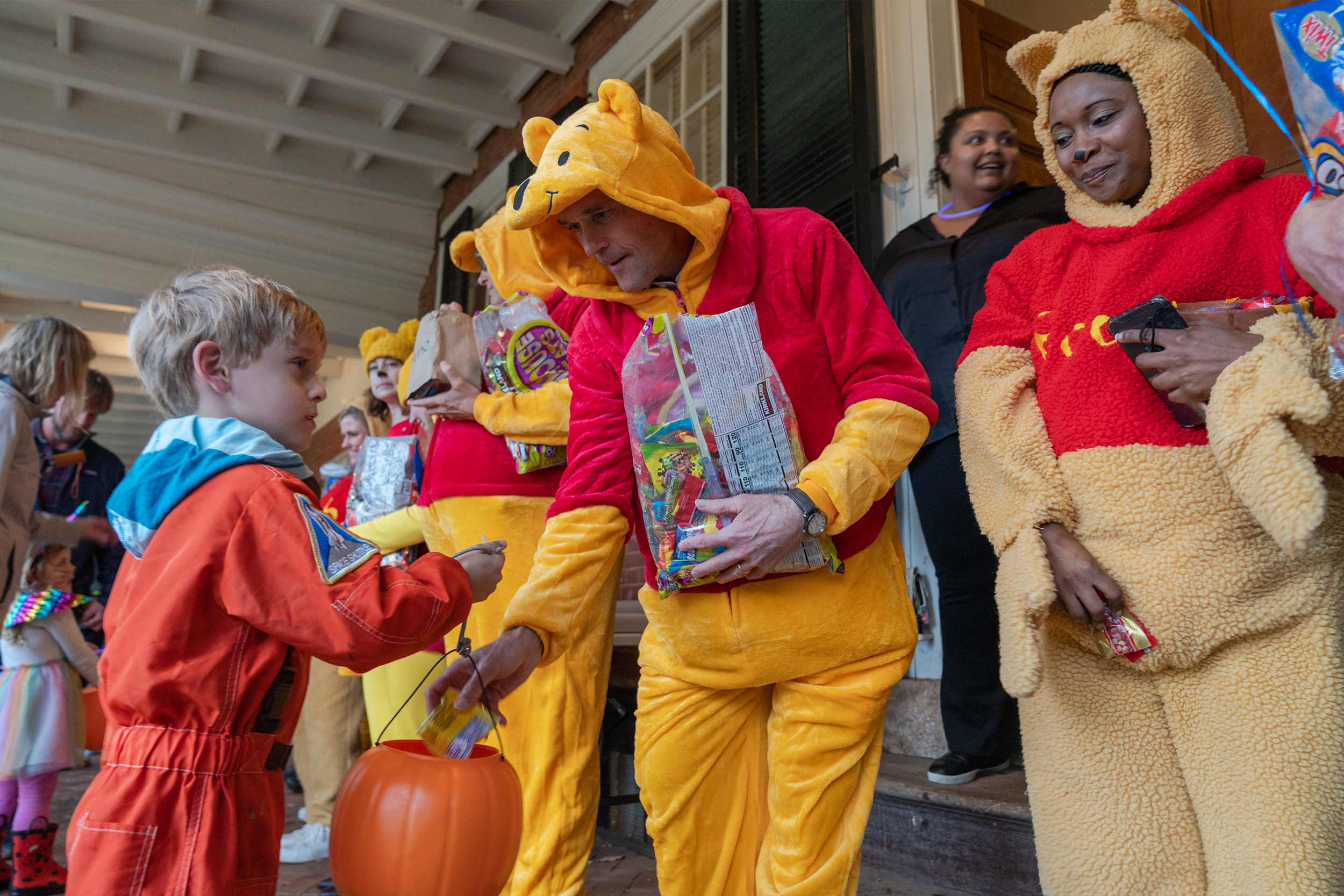 Child trick or treating with college students dressed as Winney the Pooh