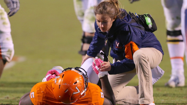 A team physician attends to a supine football player on the field