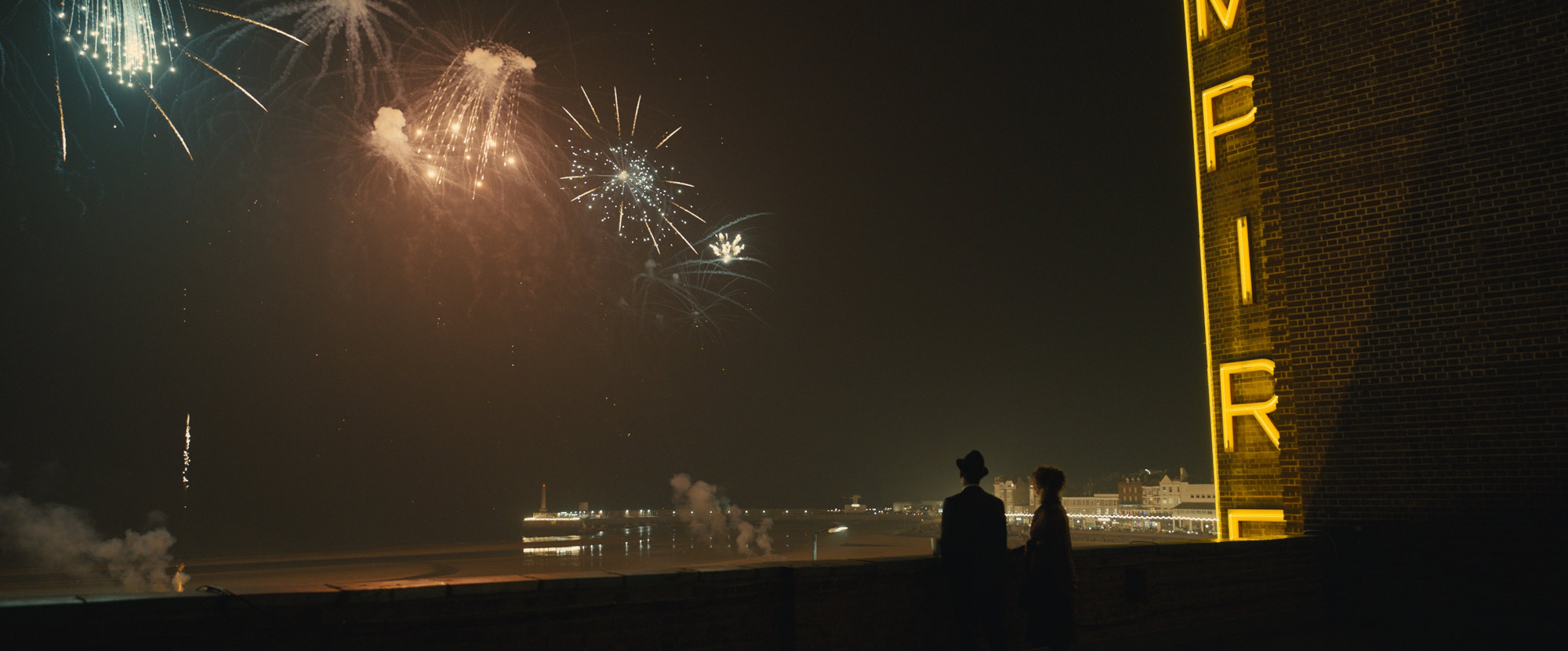 Two people watch fireworks over a body of water