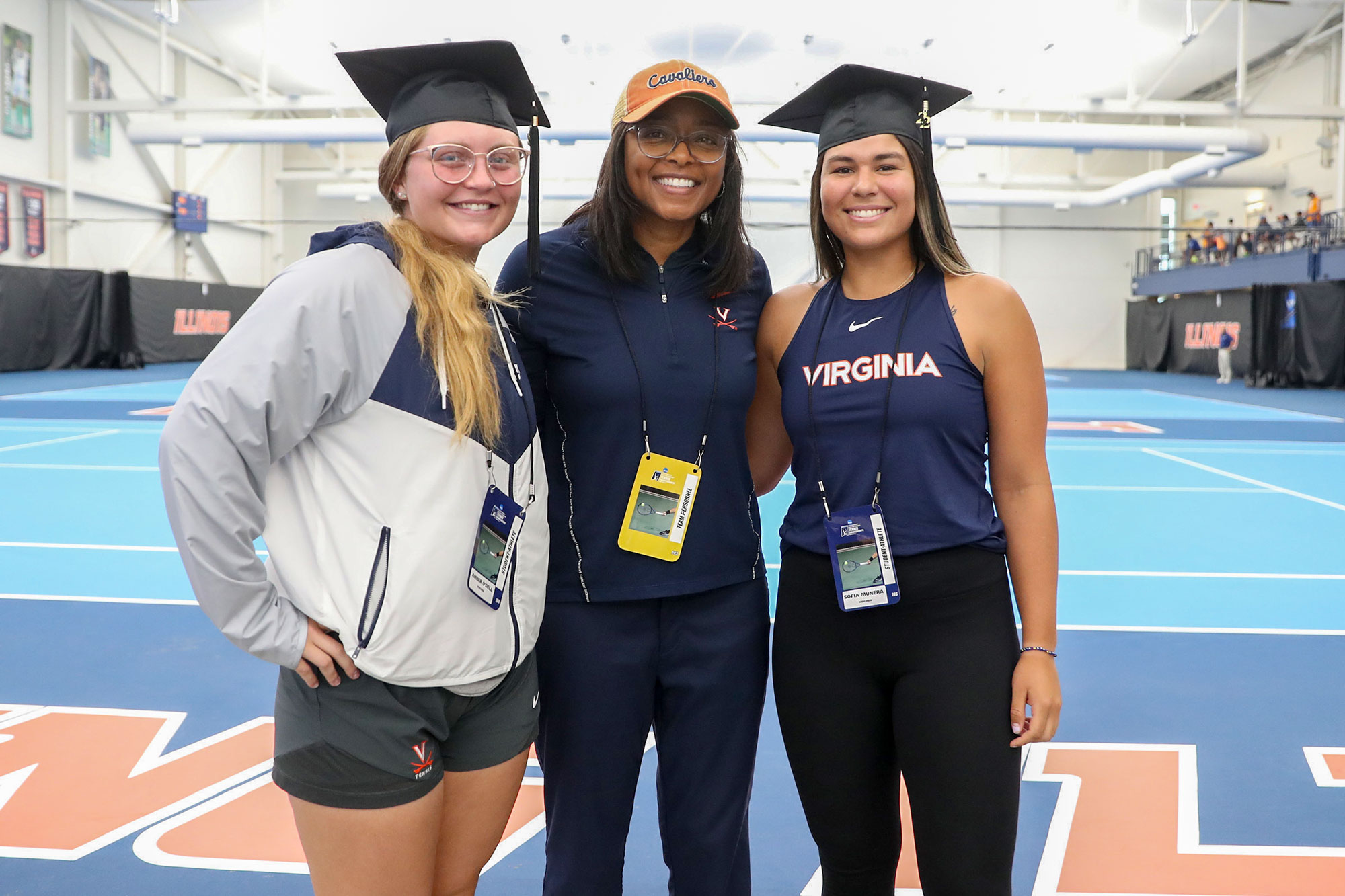 Amber O'Dell and Sofia Munera wear grad caps and pose on a tennis court with Carla Williams