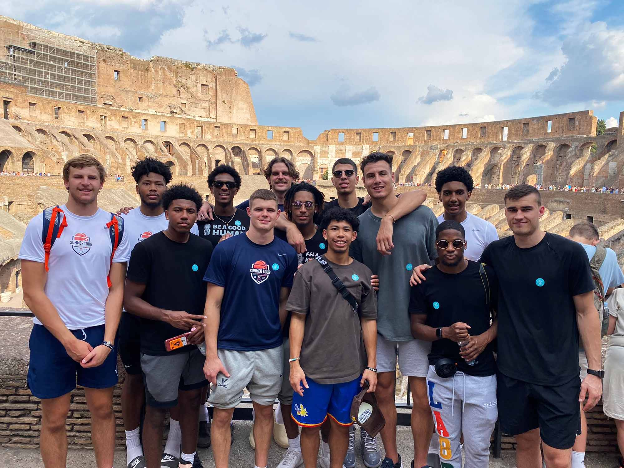 Thirteen teammates pose for a group shot in front of the Colosseum