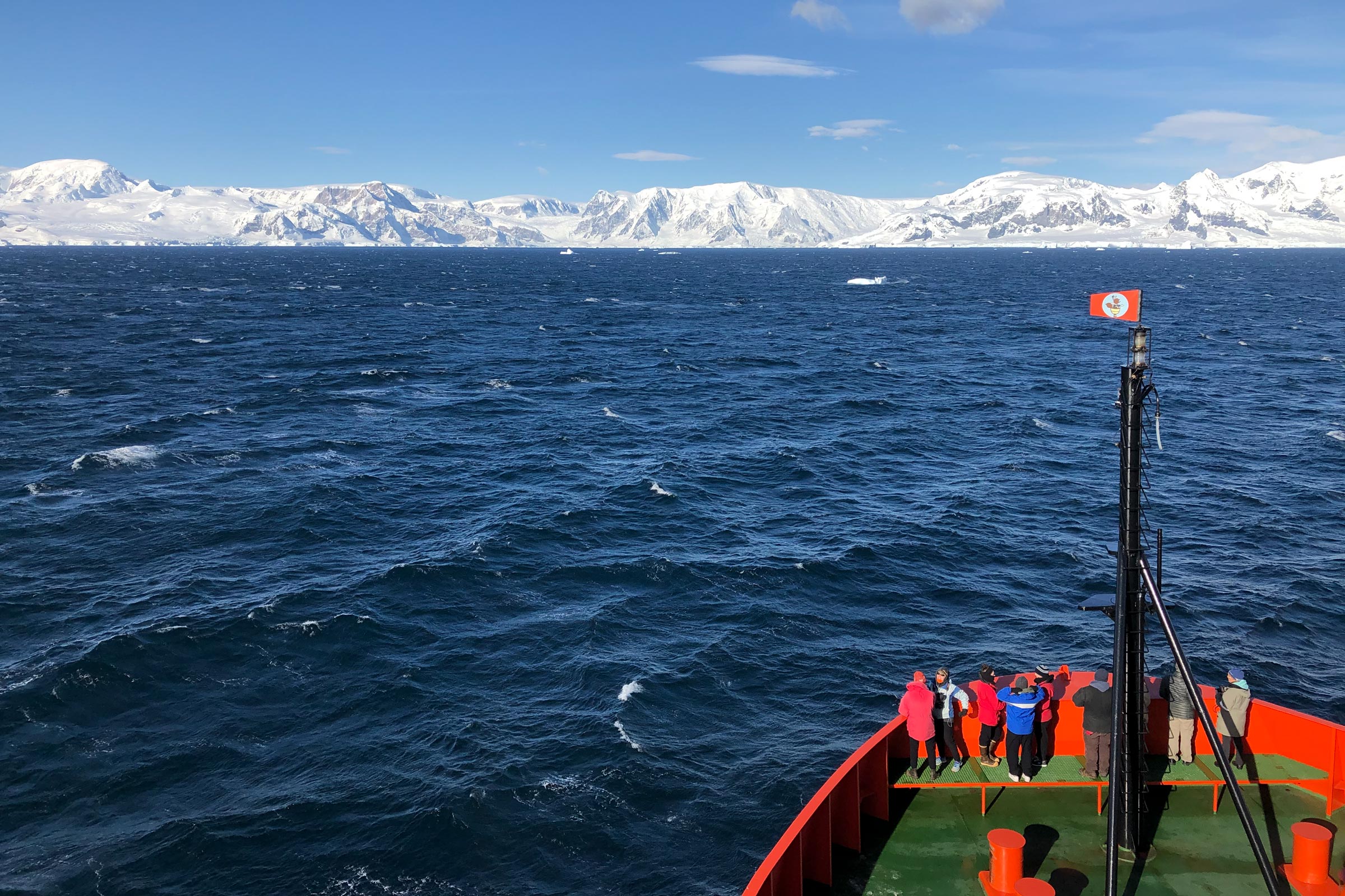 Nine researchers stand on a boat looking out over the water at the distant glacial coastline