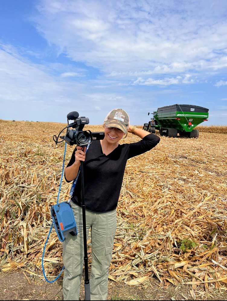 Portrait of Olivia Rinaldi holding a camera in the middle of a cornfield..