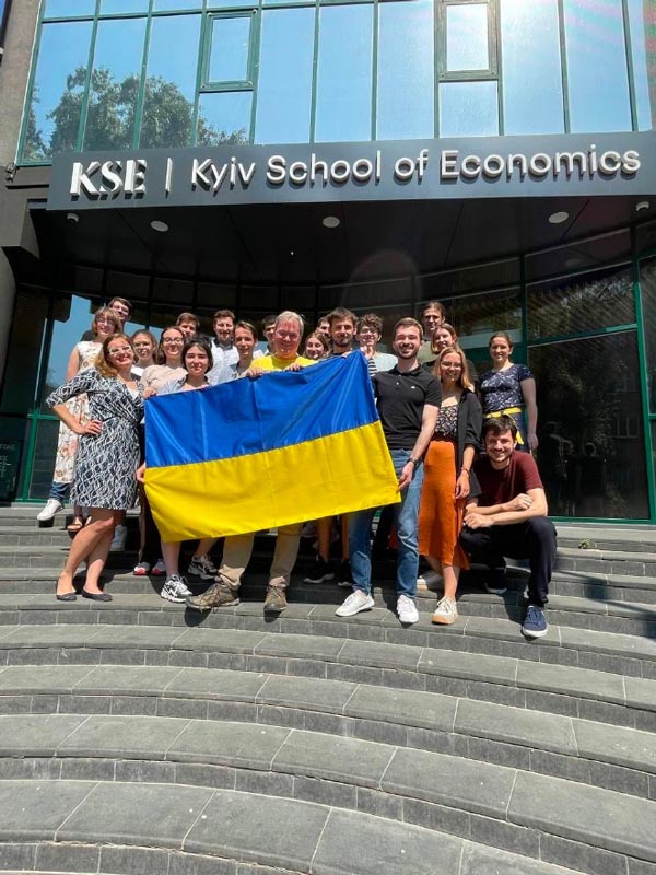 Group of people standing on steps of the Kyiv Economics building holding a Ukraine Flag