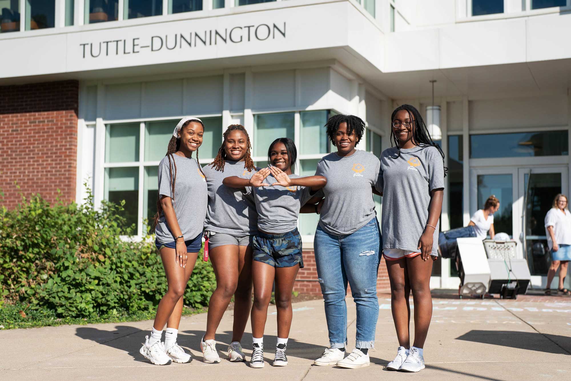 Five students wearing matching gray Greeter shirts pose in front of Tuttle-Dunnington dormitory.