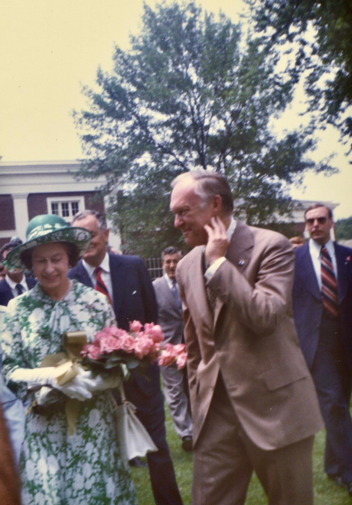 President Hereford smiles and touches his face as he walks down the Lawn with Queen Elizabeth