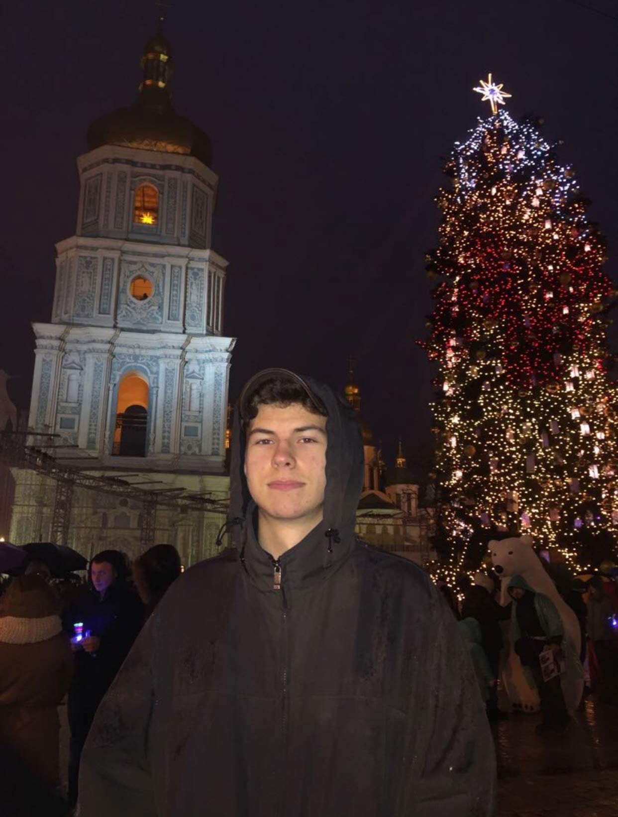 Andriy Shalkivskiy standing in front of a building and Christmas Tree in Ukraine