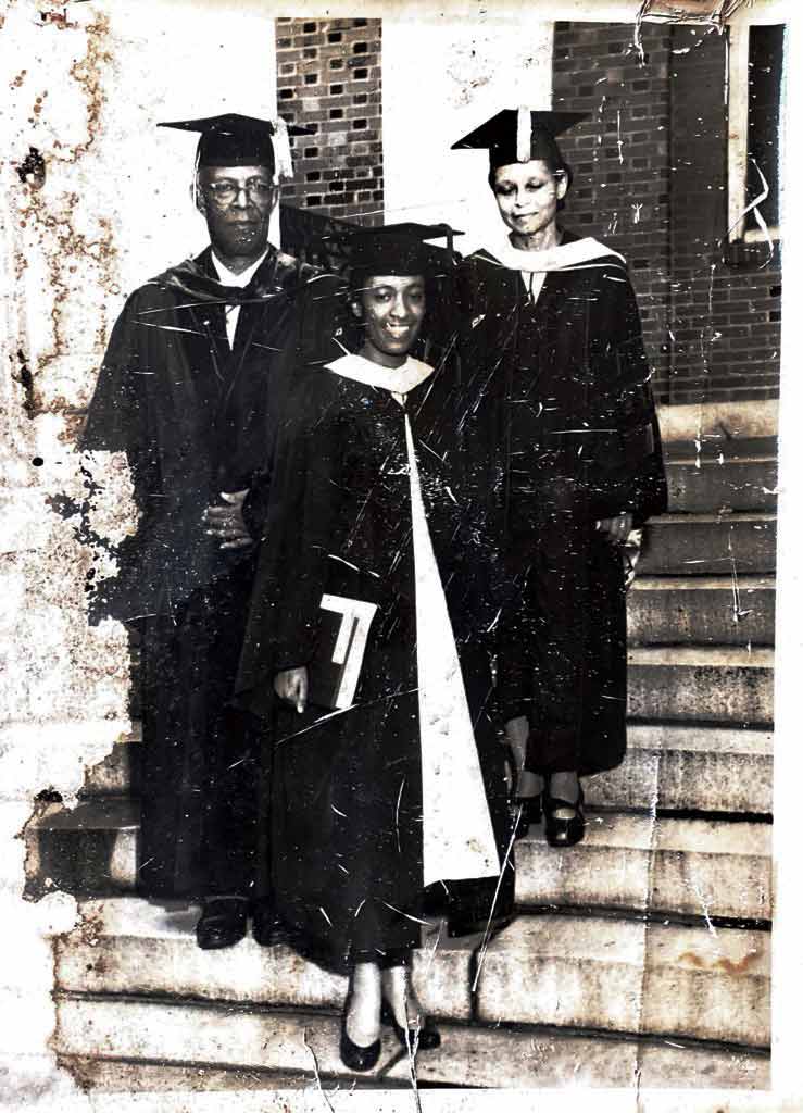 Black and white photo of three people in graduation robes posing for a portrait on a flight of stairs