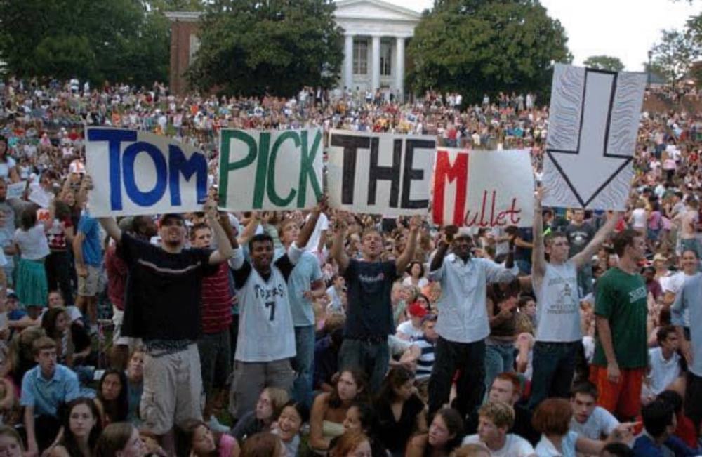 Among a huge crowd of students, five students hold up signs reading Tom Pick The Mullet