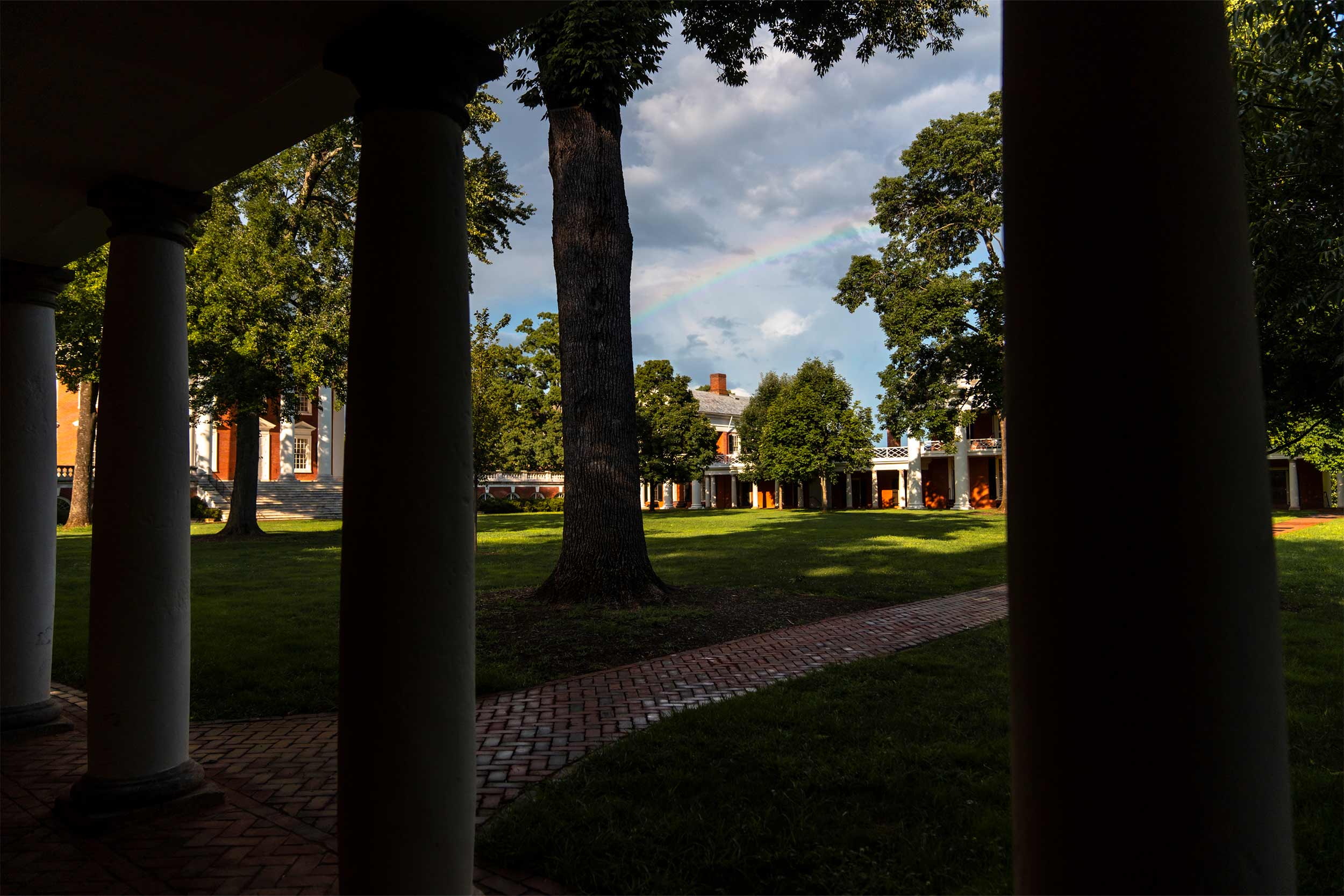 The Lawn seen through columns and trees. A rainbow is seen in the sky in the distance. 