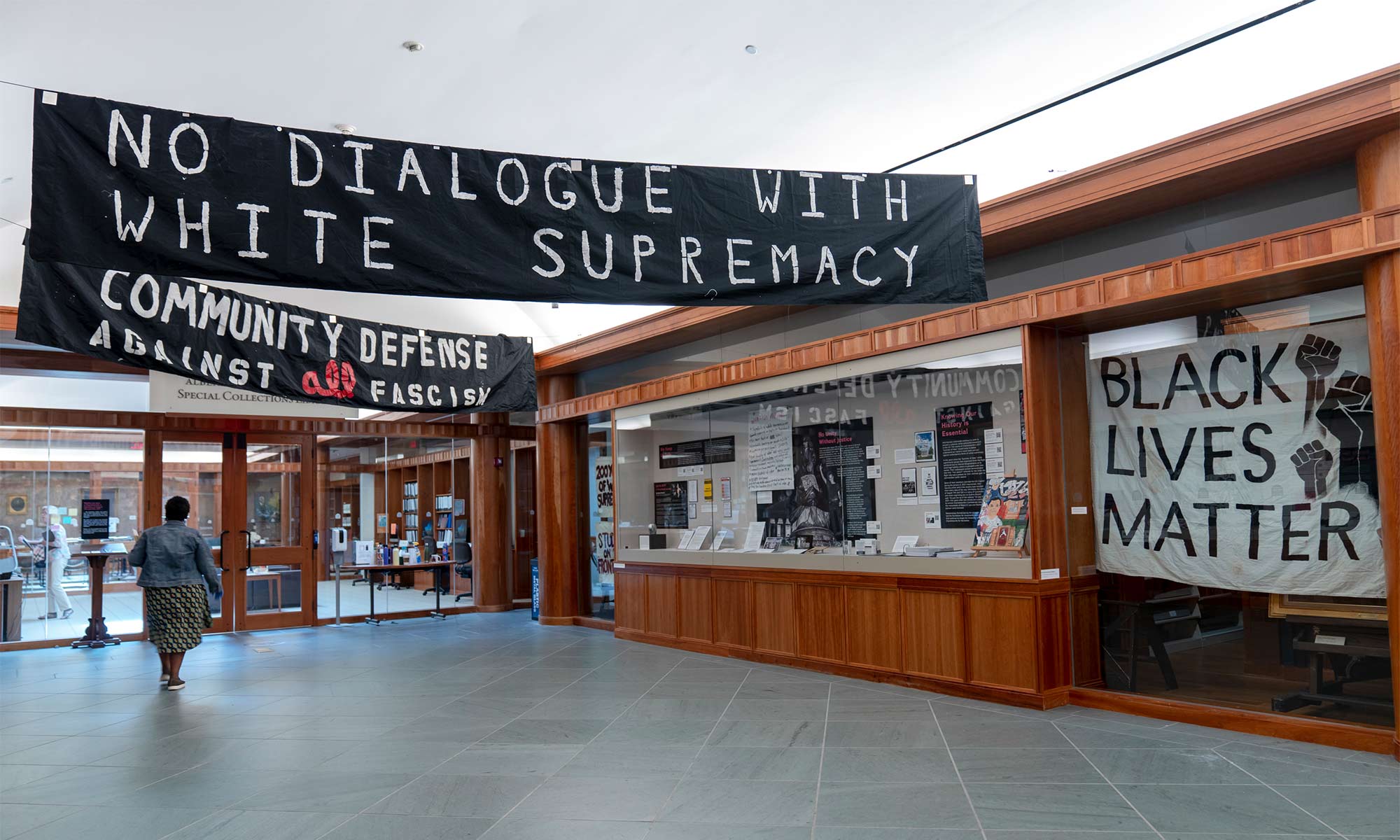 Interior photo of a display with banners that read "No dialogue with white supremacy" and "Community defense against fascism" and "Black lives matter"