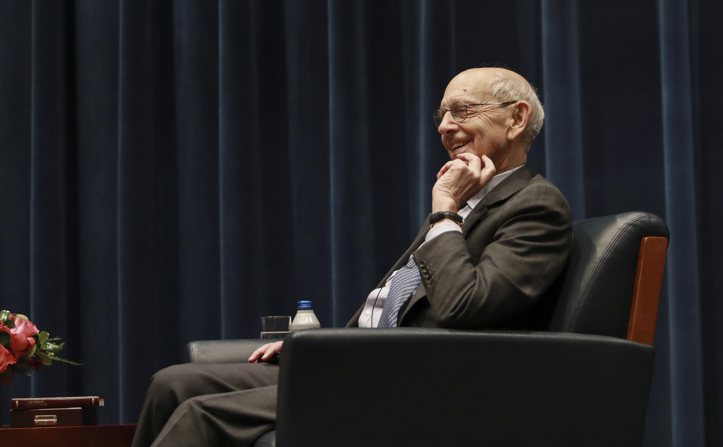 Breyer, seated in a leather chair, smiles and scratches his chin.