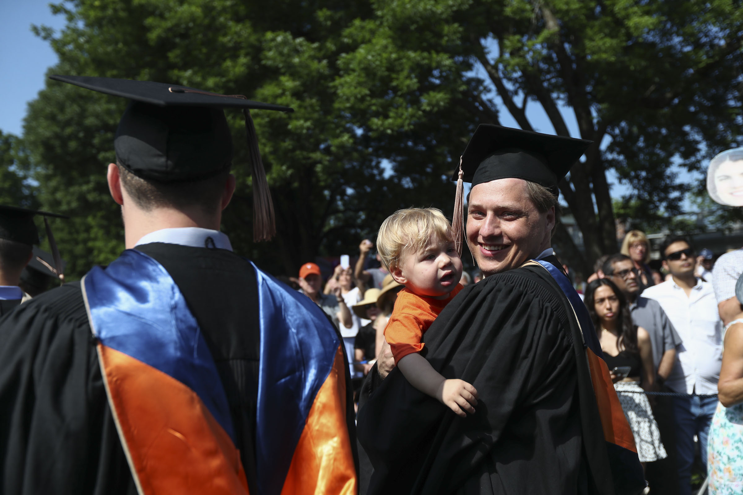 A student embraces a toddler as he and more than 4,500 of his classmates make their way down the Lawn.