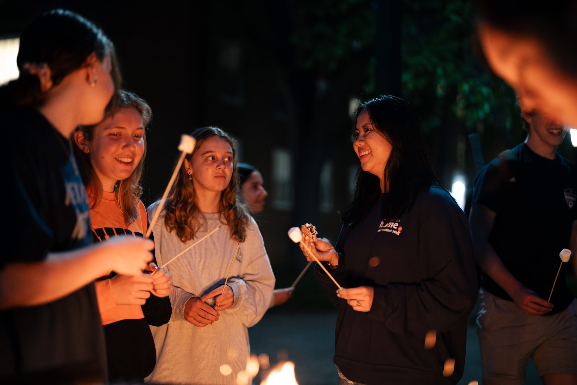 Students hold sticks with marshmallows as they chat with Dao Tran around a fire
