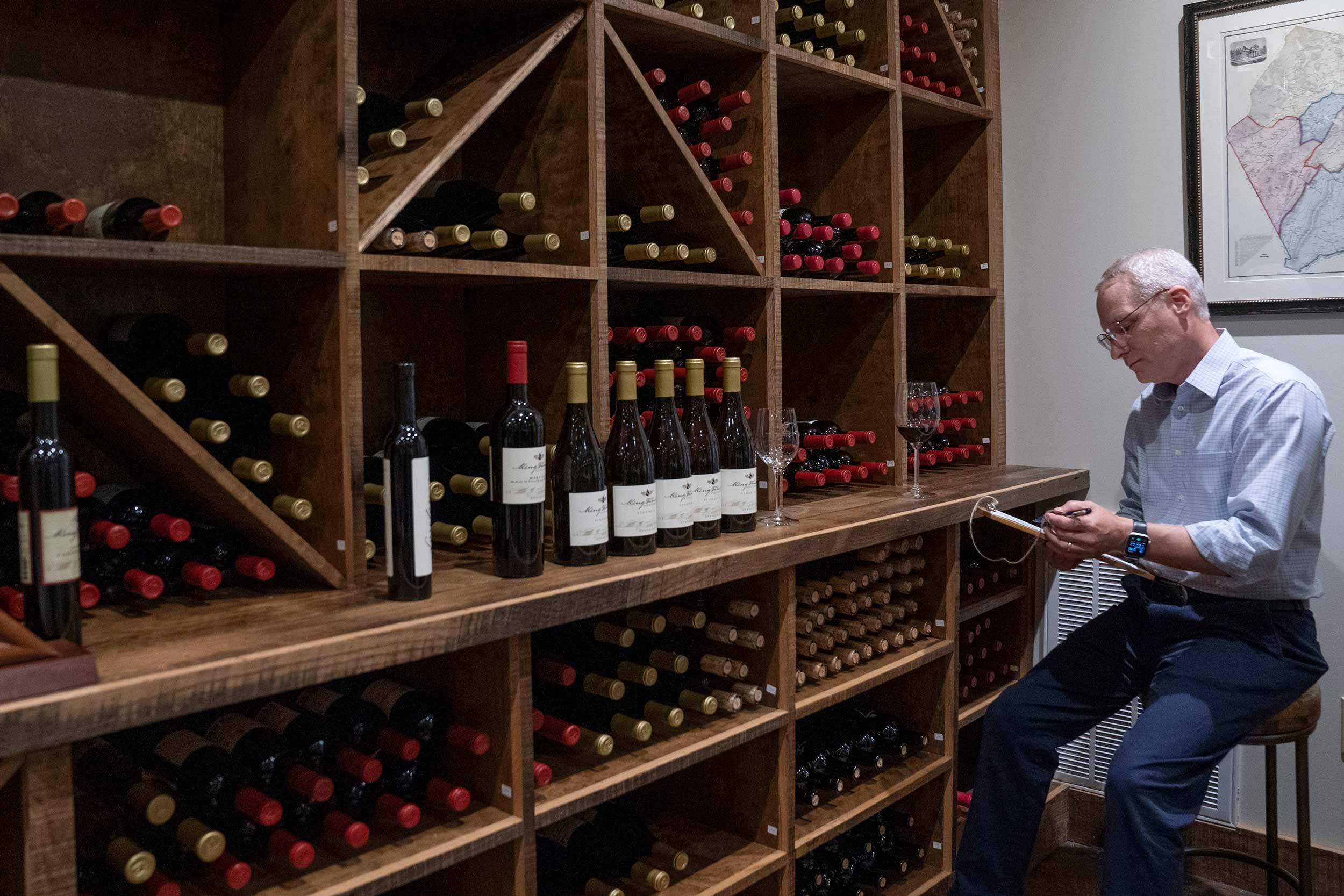Rodney Sullivan sitting on a chair reading a lable on a bottle of wine in a wine cellar