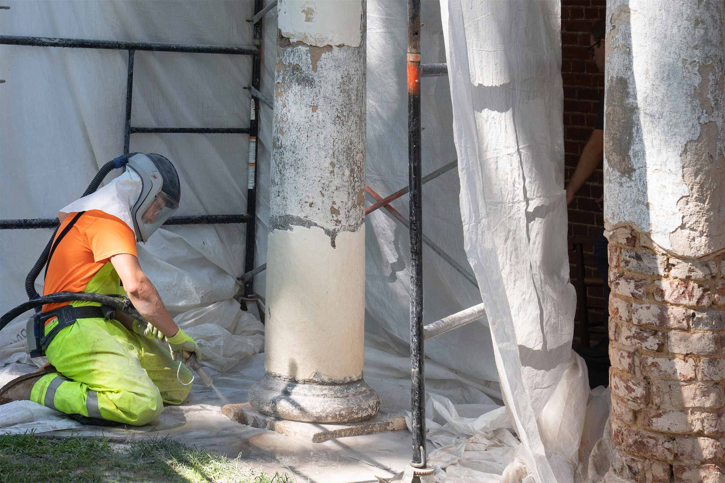 Construction worker kneeling down next to column with face covering