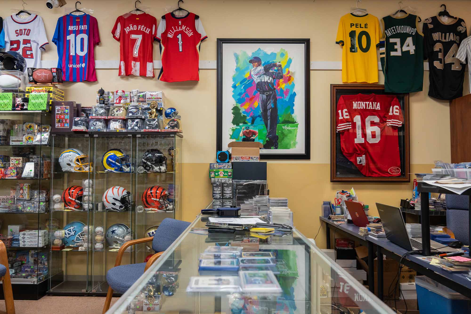 The interior of the shop includes a glass display case full of cards and other memorabilia, as well as hanging jerseys and shelves of football helmets