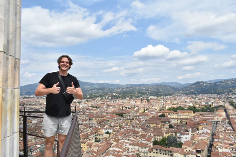 Ben Vander Plas poses with two thumbs up in front of the Italian landscape.