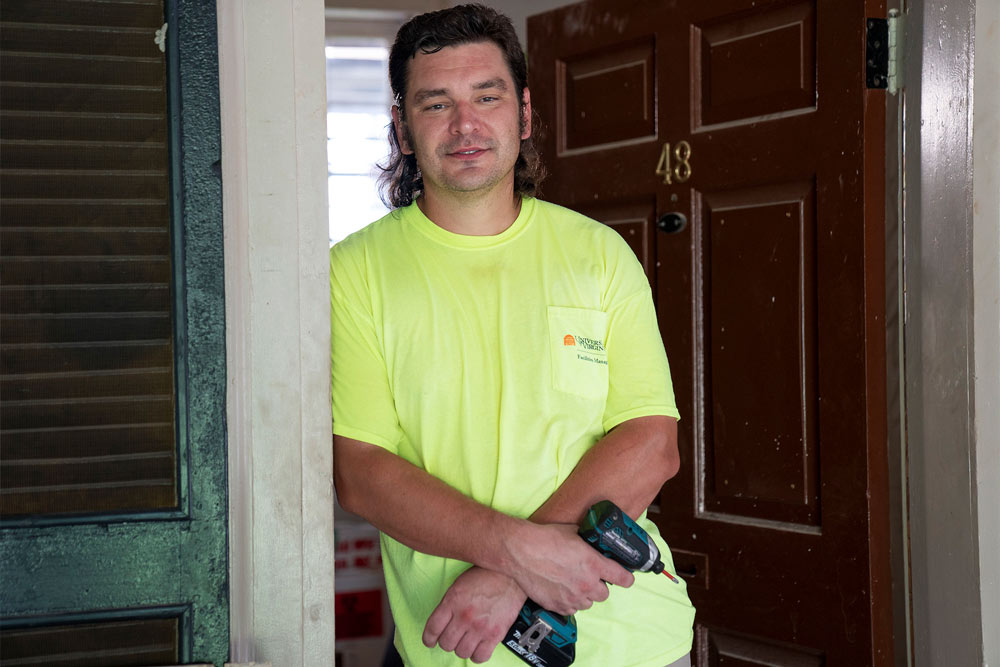 Andrew Shelton stands in the doorway of Room 48 on the Lawn holding a drill. 