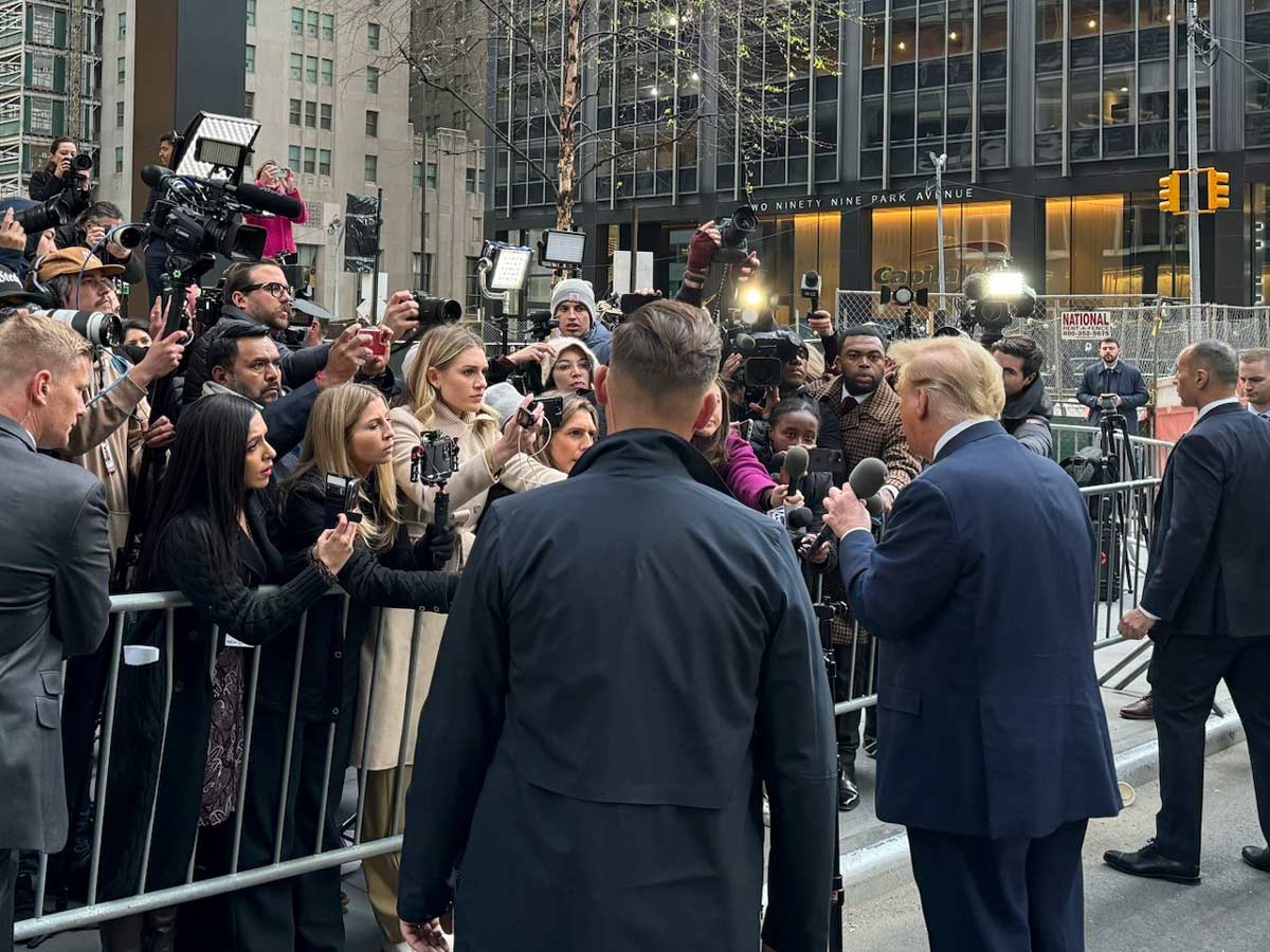 A candid portrait of President Donald Trump during a rally, with a large number of reporter asking questions.