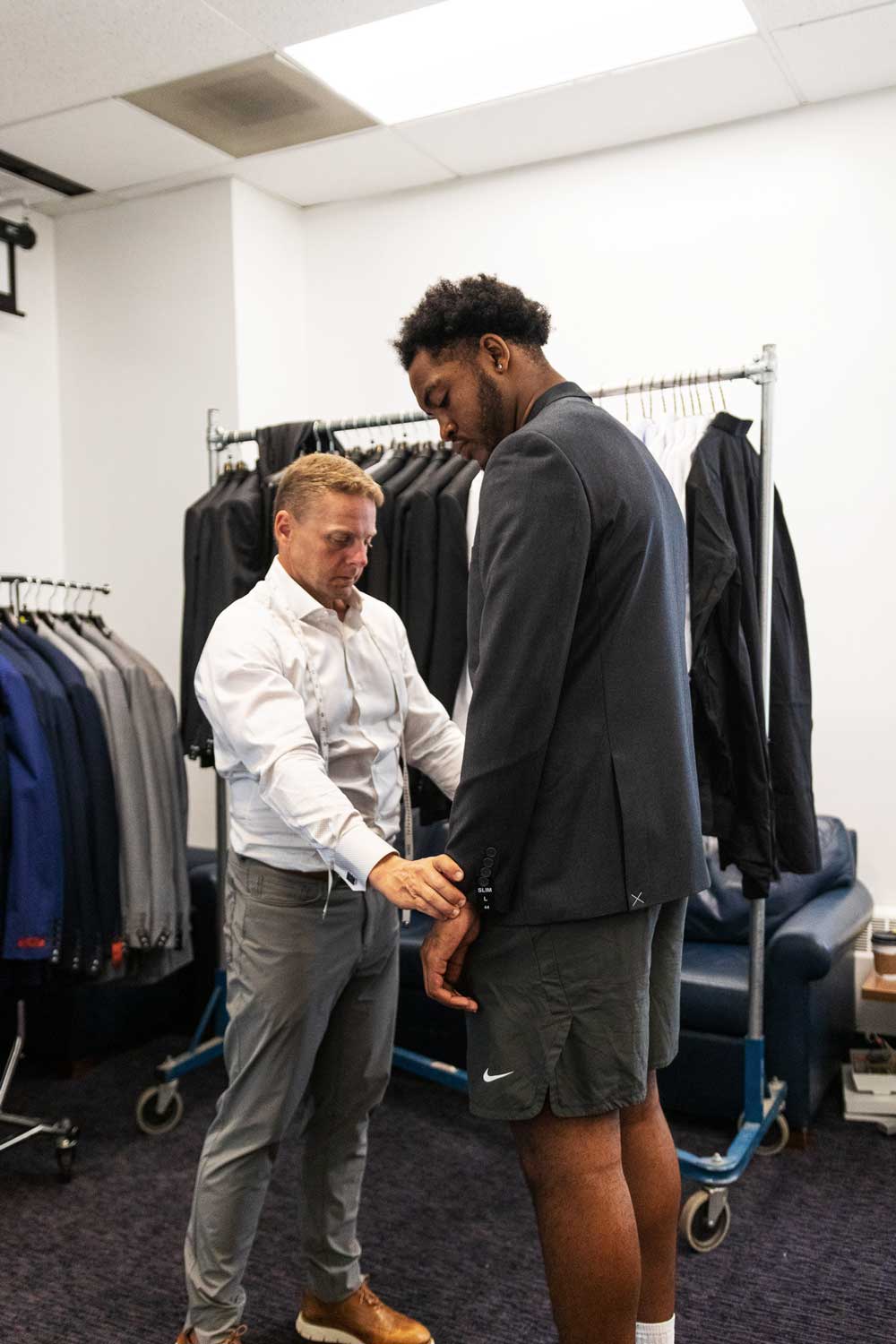 In a suit shop, a man checks the fit of a suit worn by a football player