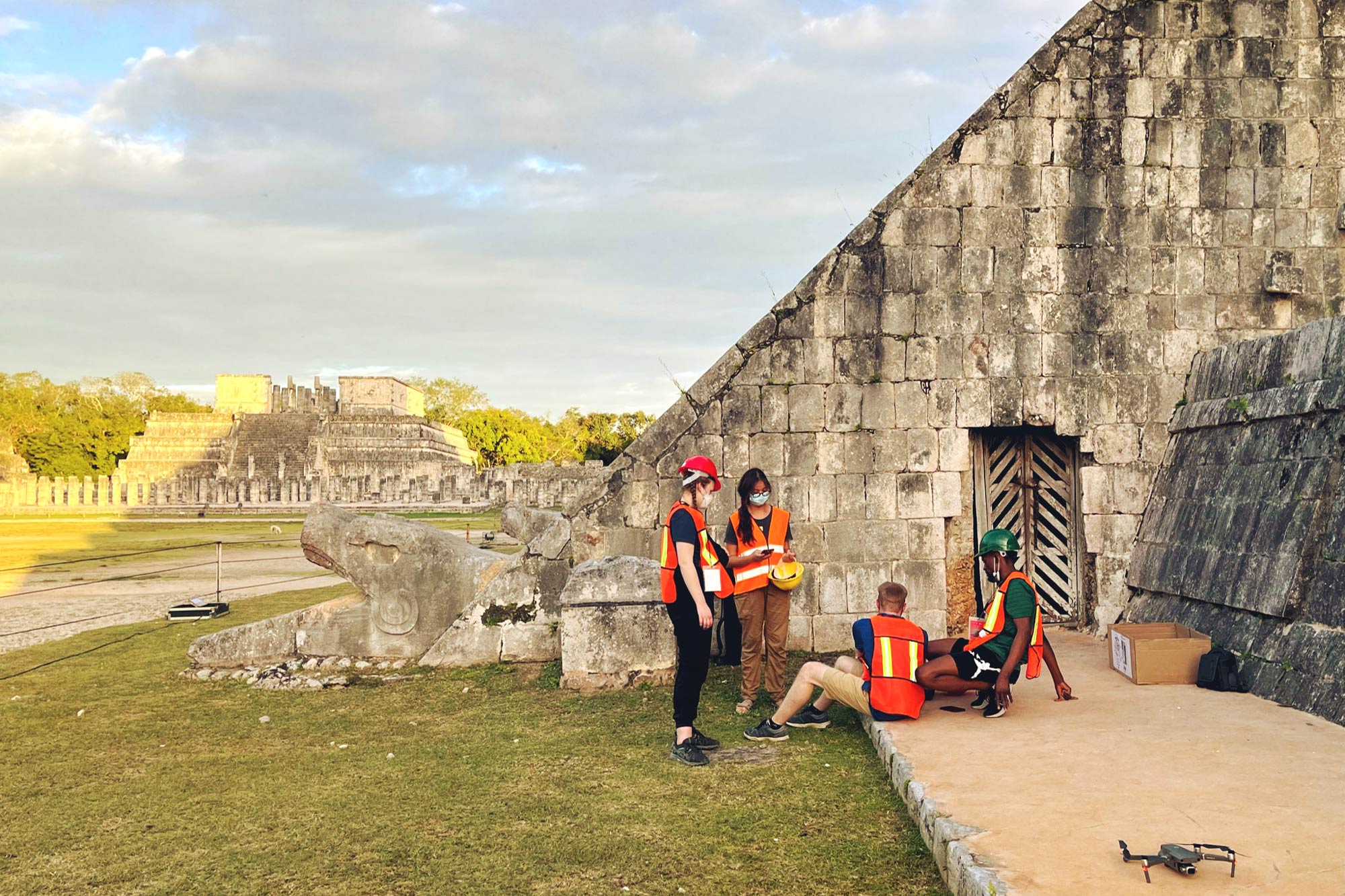 Four people in orange vests and hard hats relax near an entrance at the base of the pyramid.