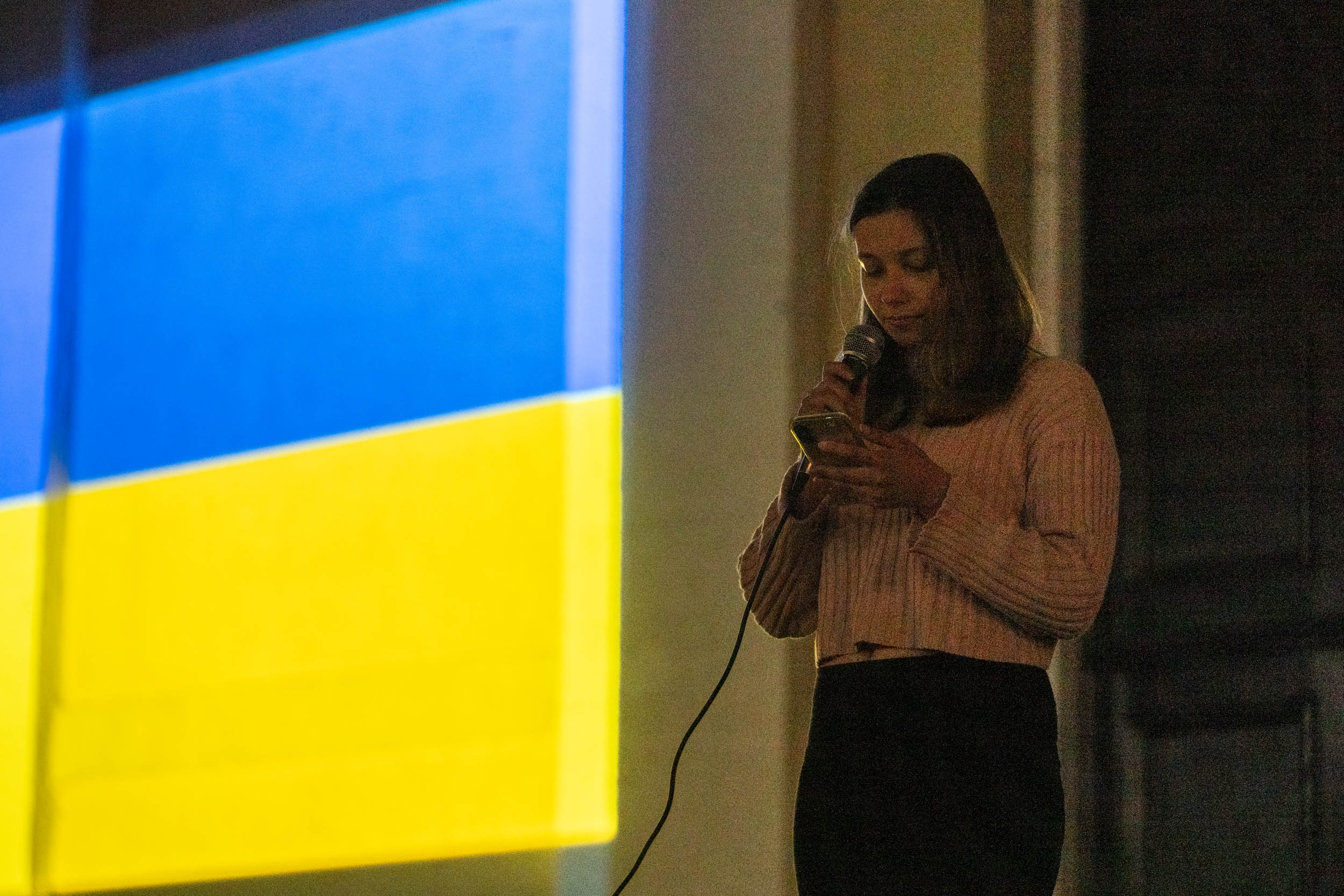 Woman standing with microphone with Ukraine flag next to her during the Ukraine vigil