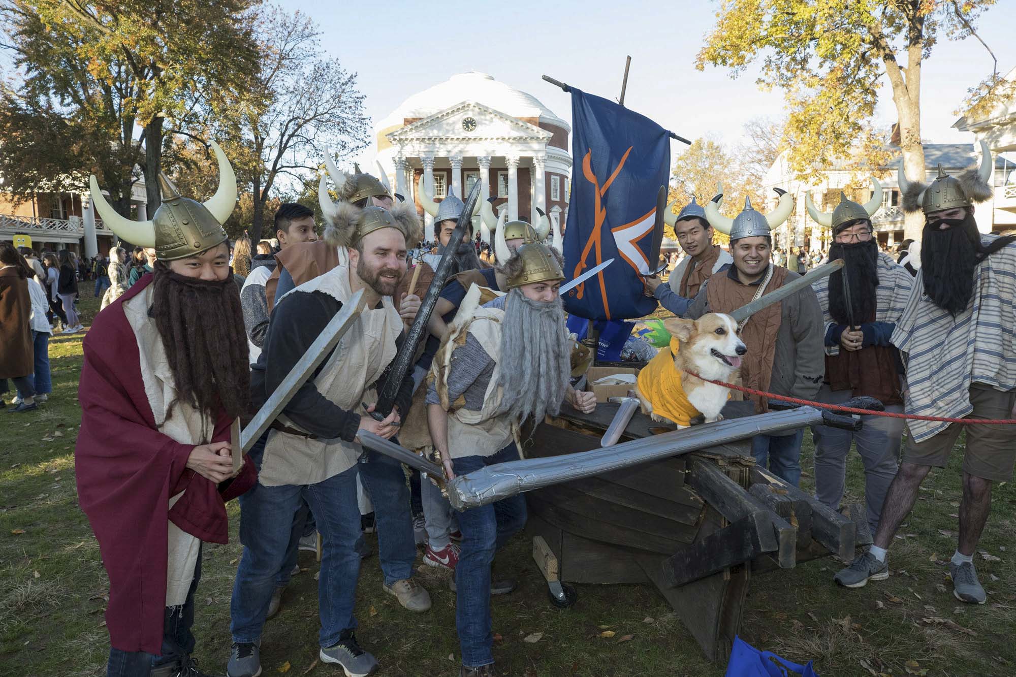 People in Viking costumes on the lawn pose with a corgi in a yellow shirt