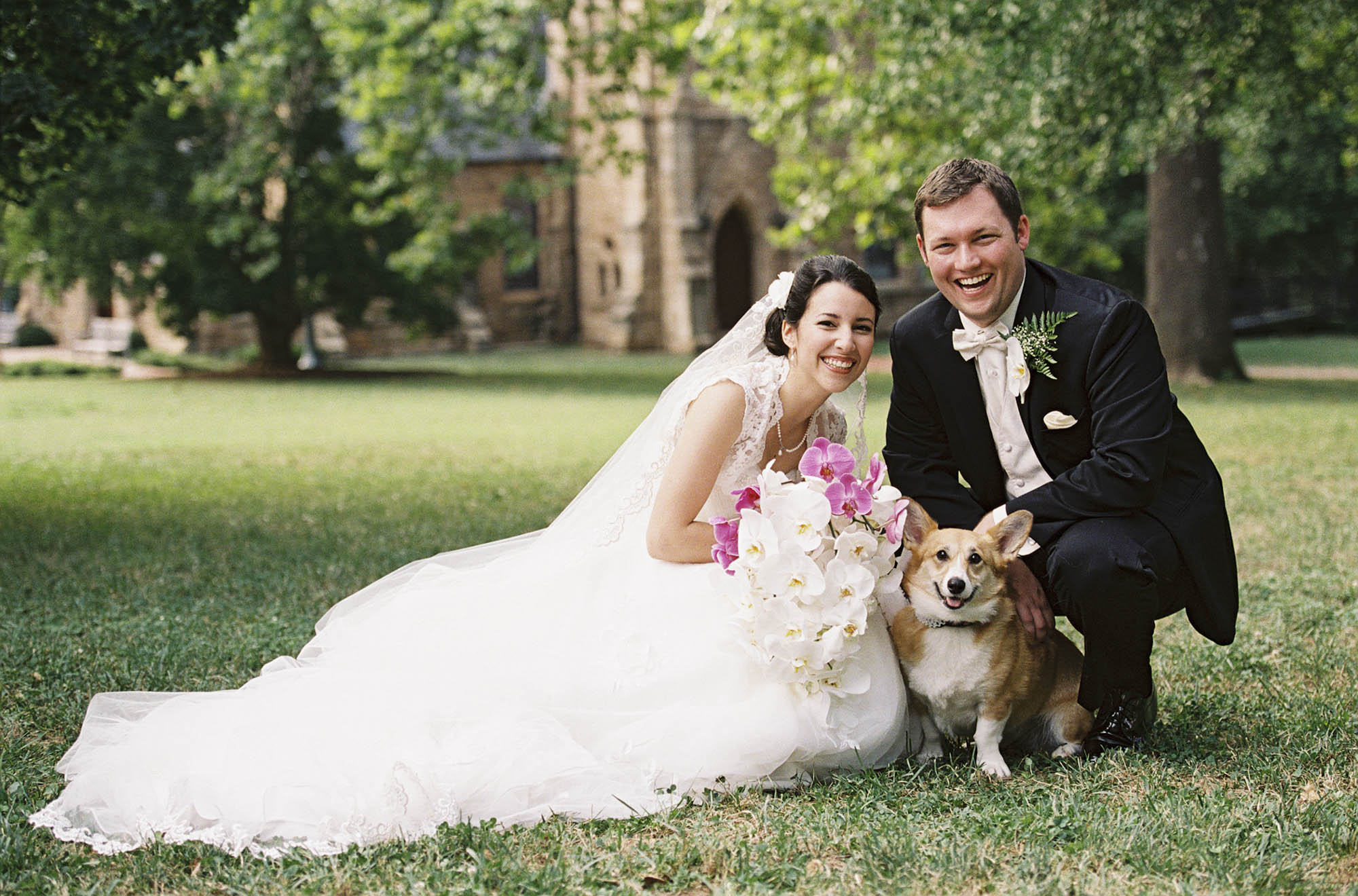 A bride and groom pose in front of the UVA Chapel with a corgi