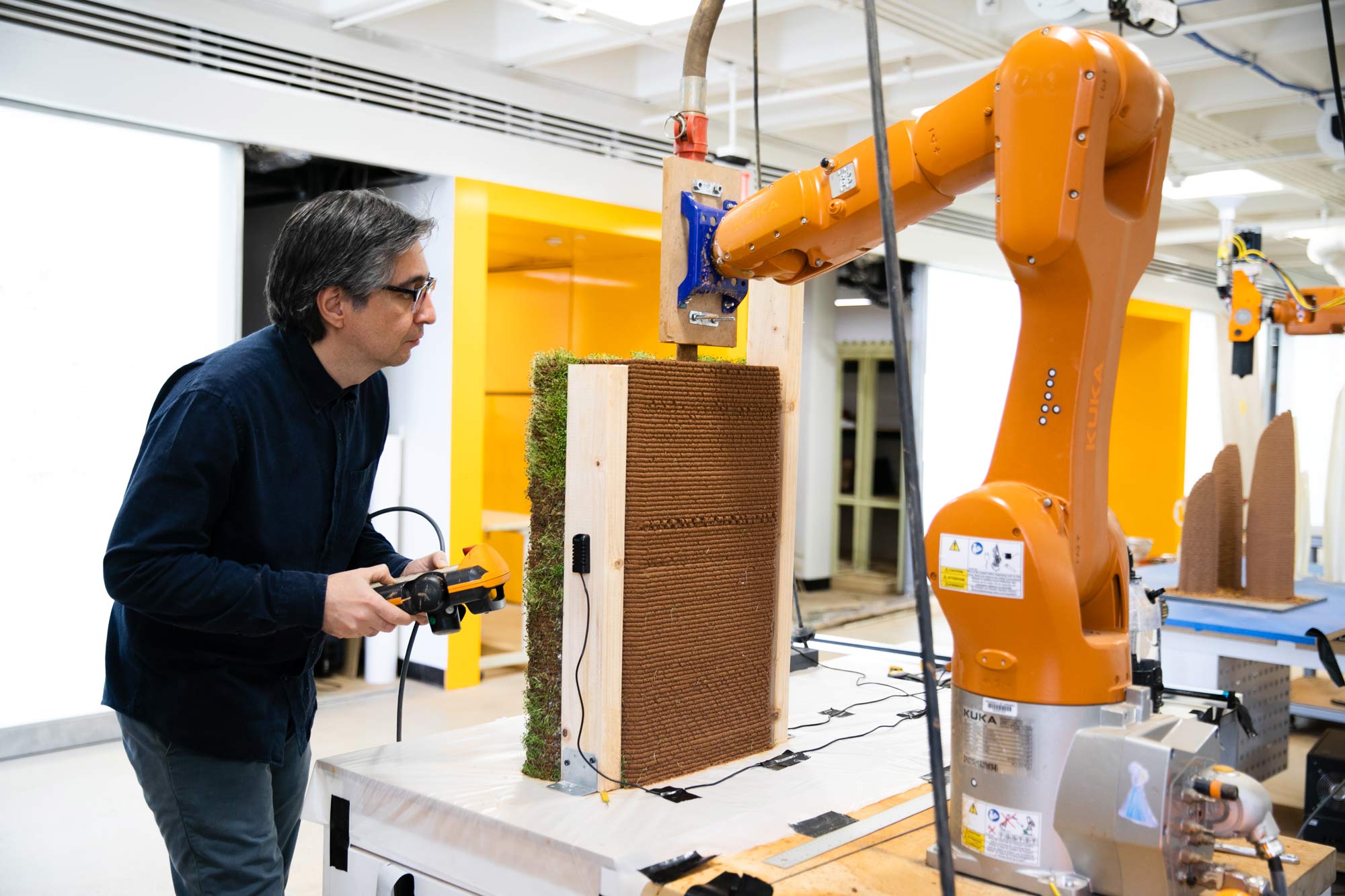 A man holds a controller and examines a robotic arm