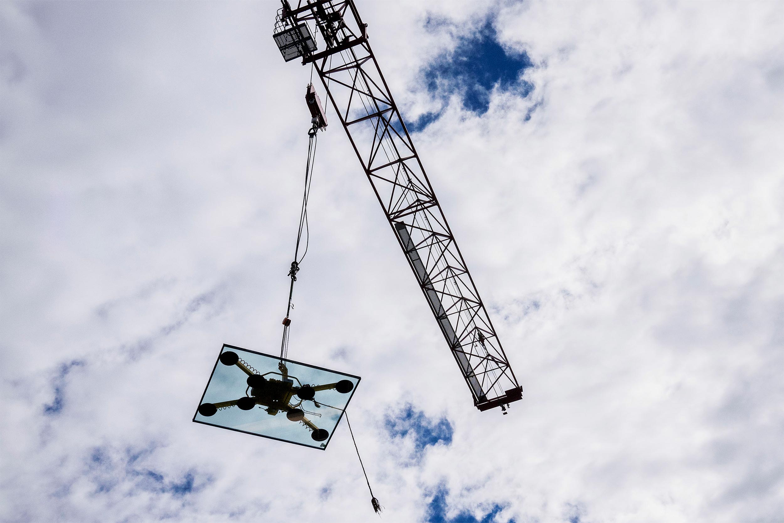 Against a partly cloudy sky, a crane lowers a pane of glass
