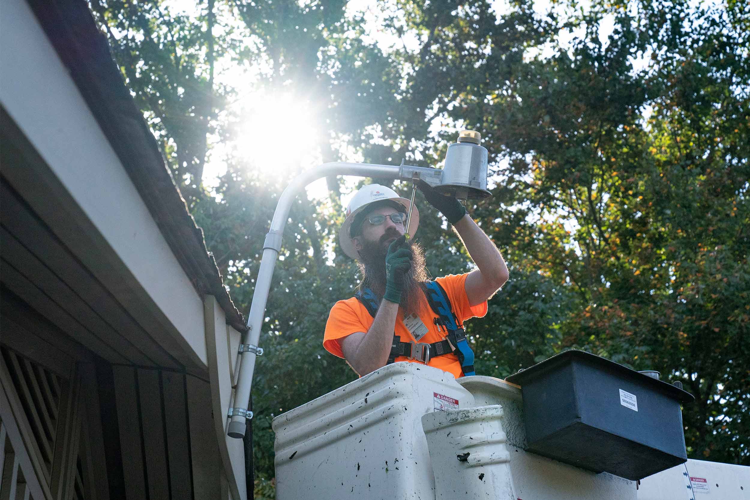A man in a bucket lift uses tools to fix an exterior light.