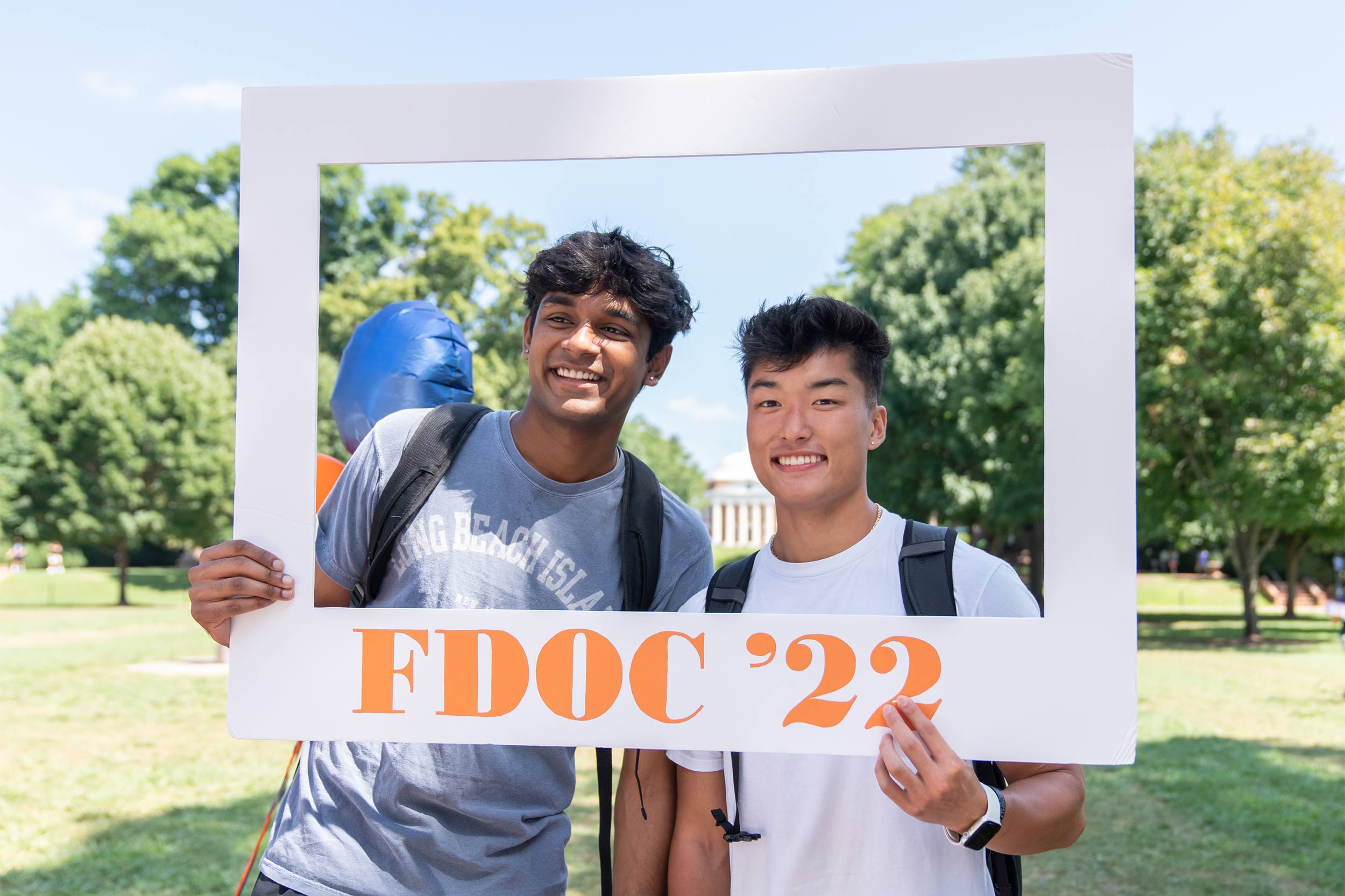 Two smiling students wearing backpacks hold a frame reading FDOC '22