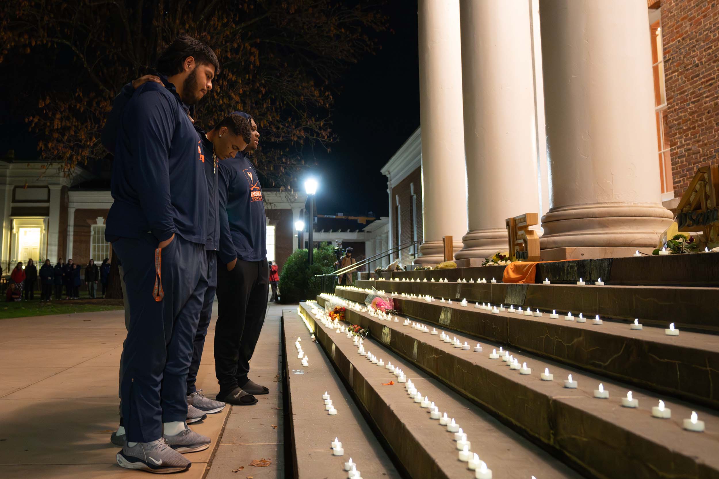 Three football players standing at the base of the stairs of Old Cabell Hall, the stairs are covered with tiny candles