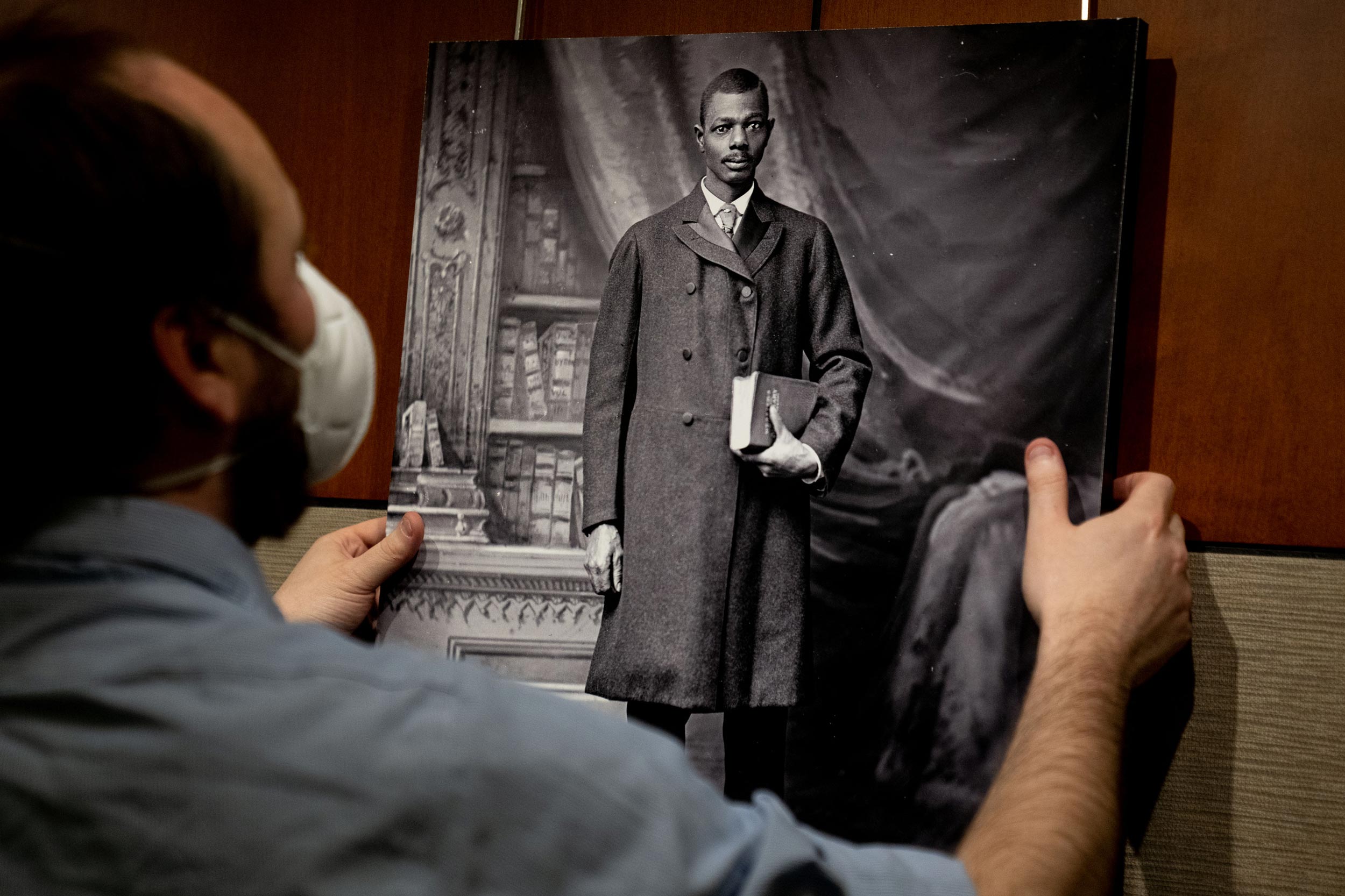 Northside librarian Evan Stankovics holds a black and white portrait of a Black man in a double-breasted coat, holding a book