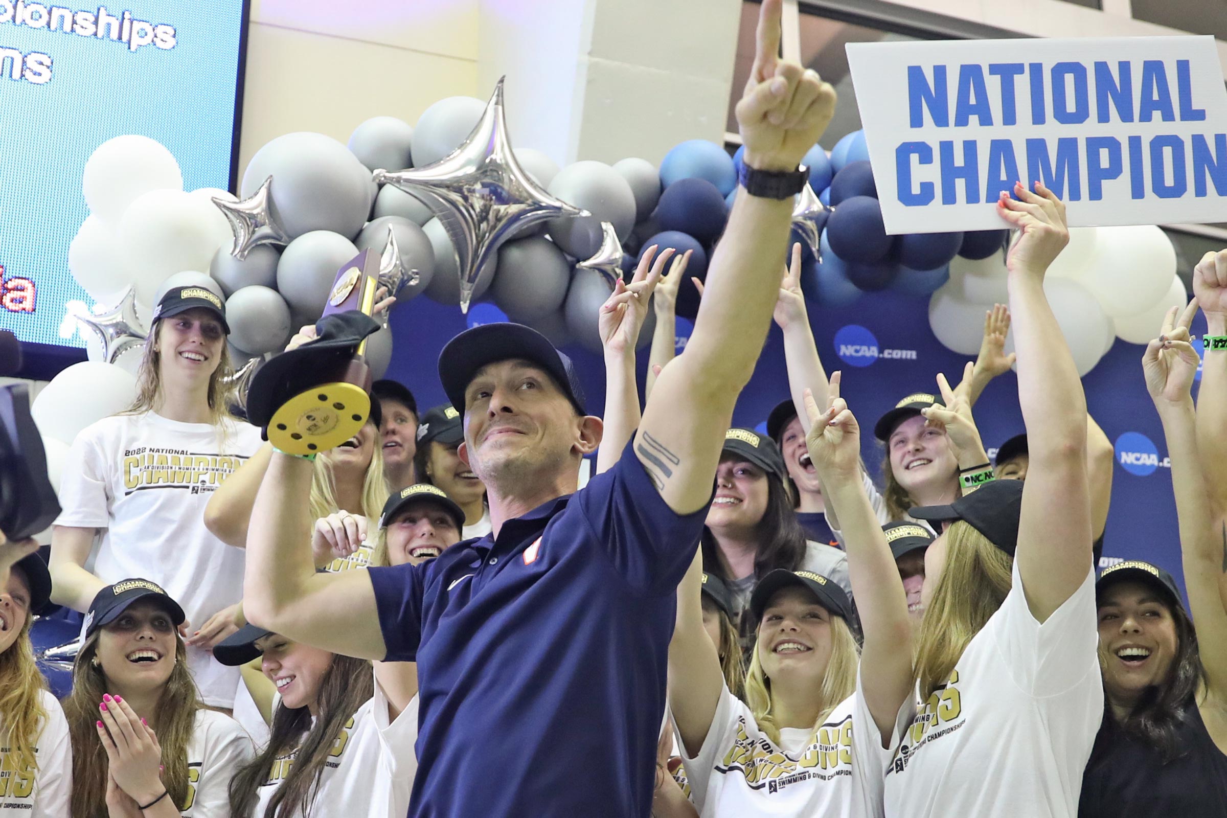 Todd Desorbo and the UVA women's swimming team raising their hands and smiling with balloons and a sign reading "National Champions"