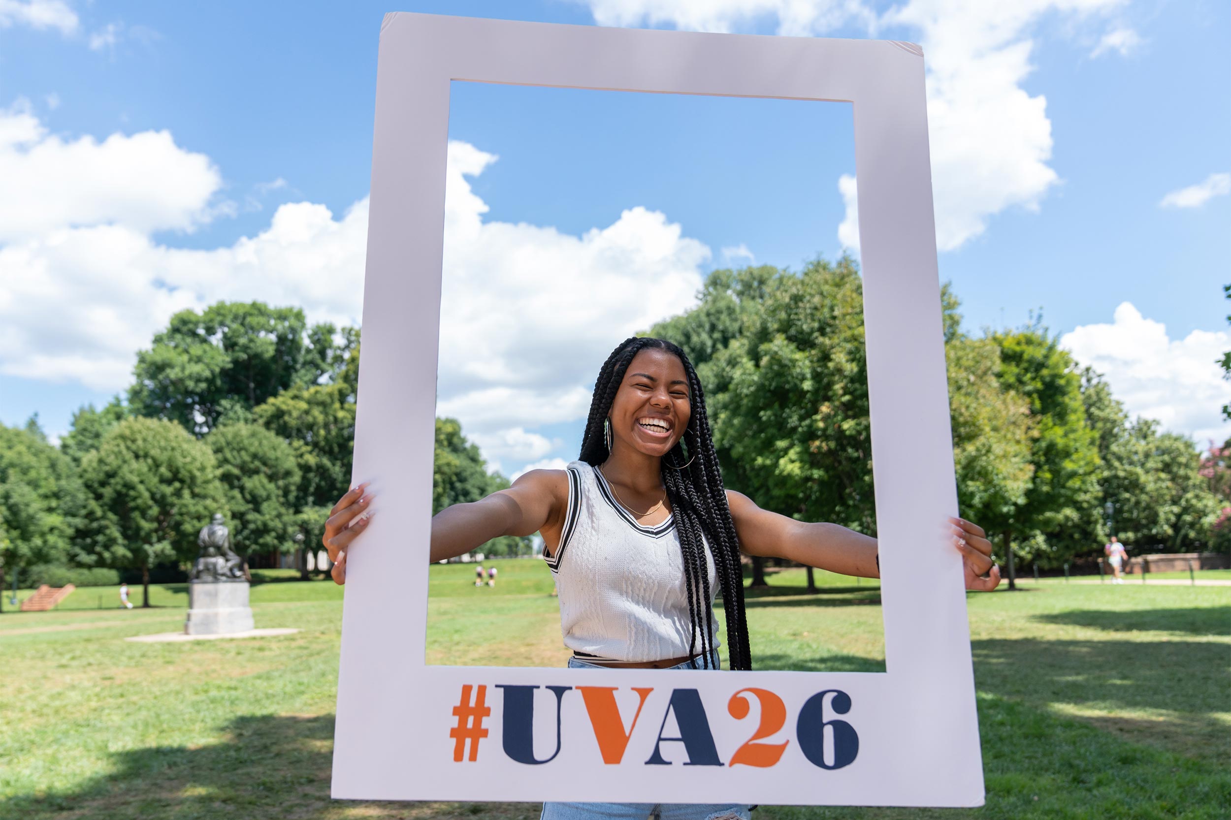 A smiling student holds a frame reading #UVA26