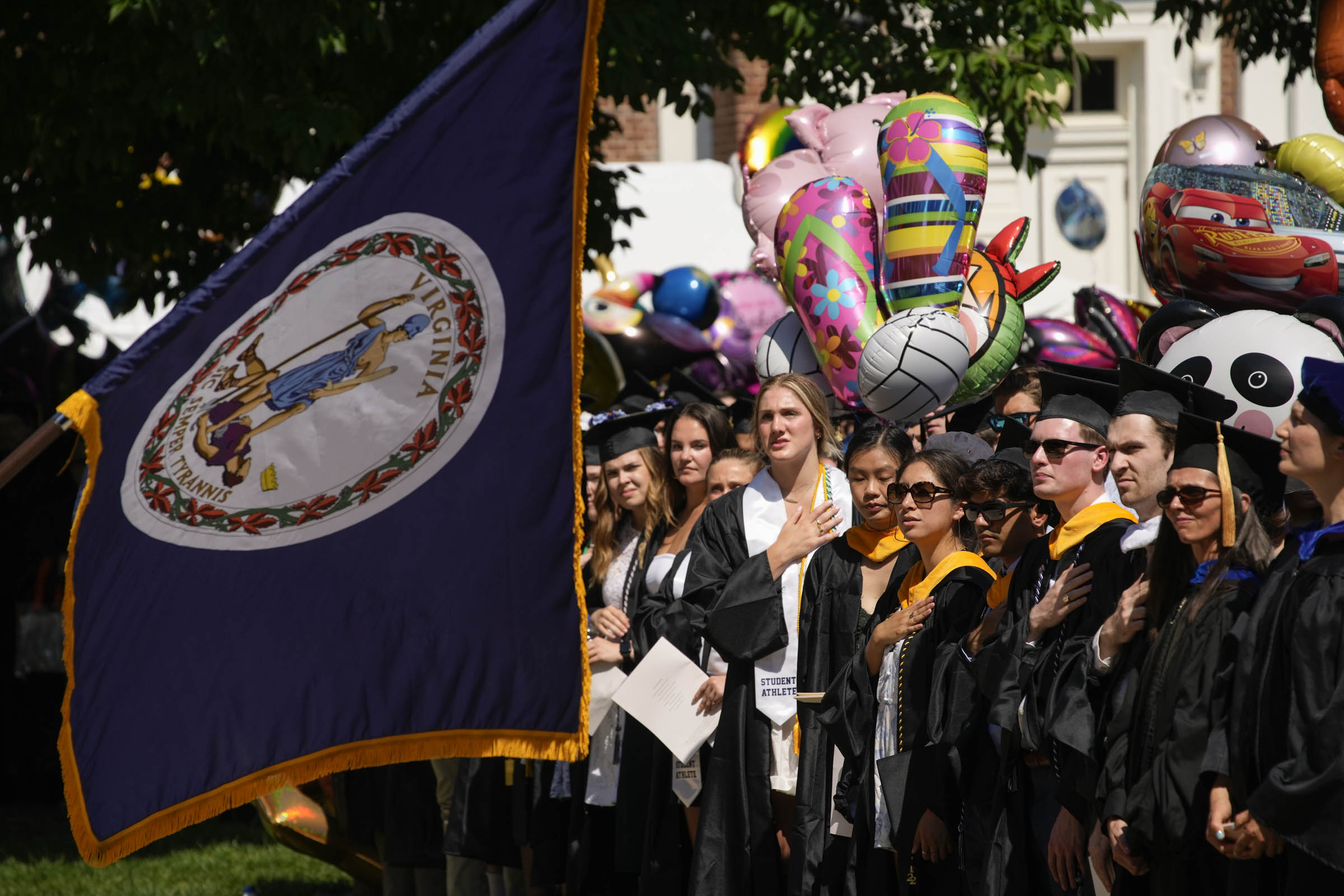 A row of graduating students with their hands on their hearts is visible behind the Virginia flag