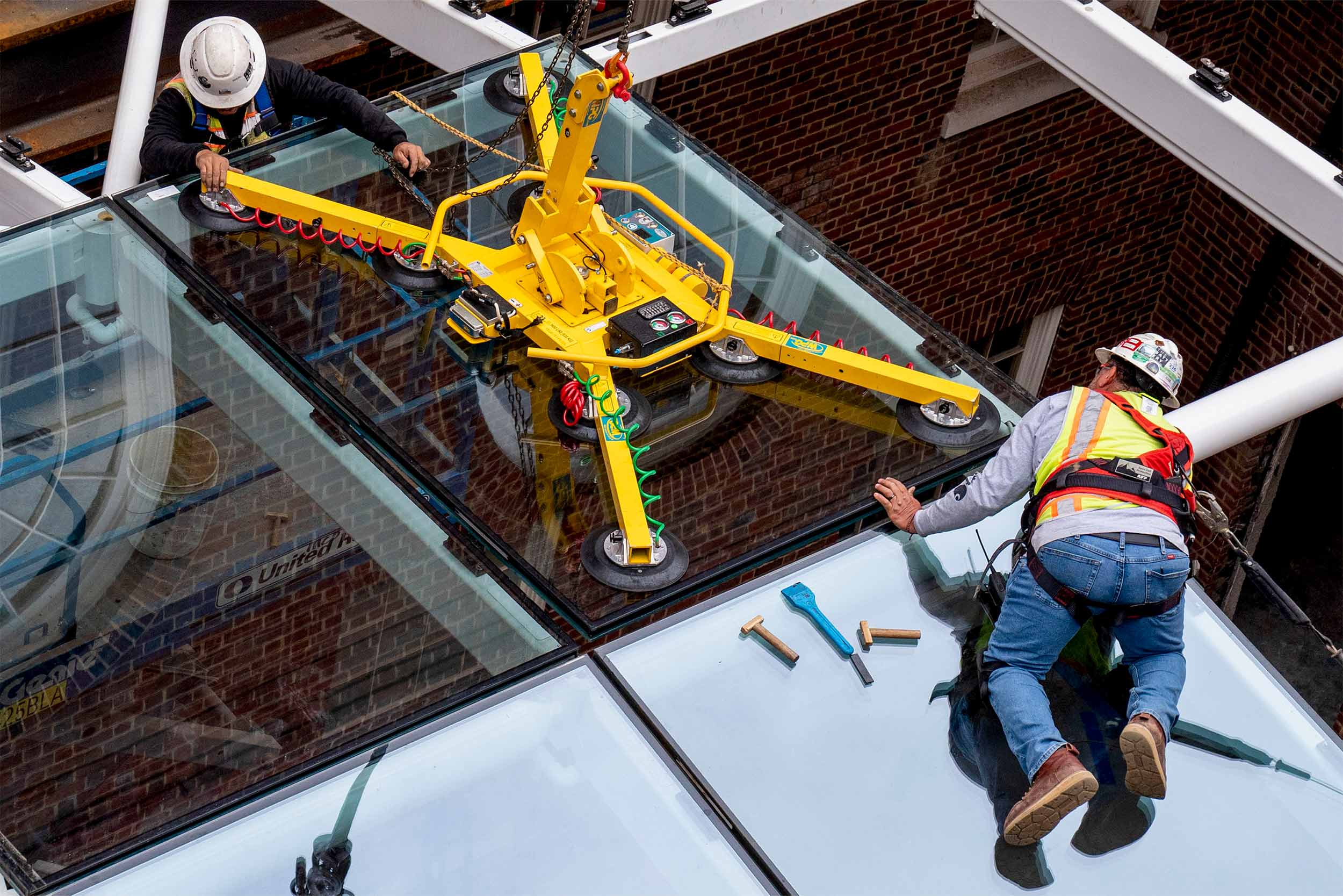 On hands and knees, two workers guide the pane of glass into the frame