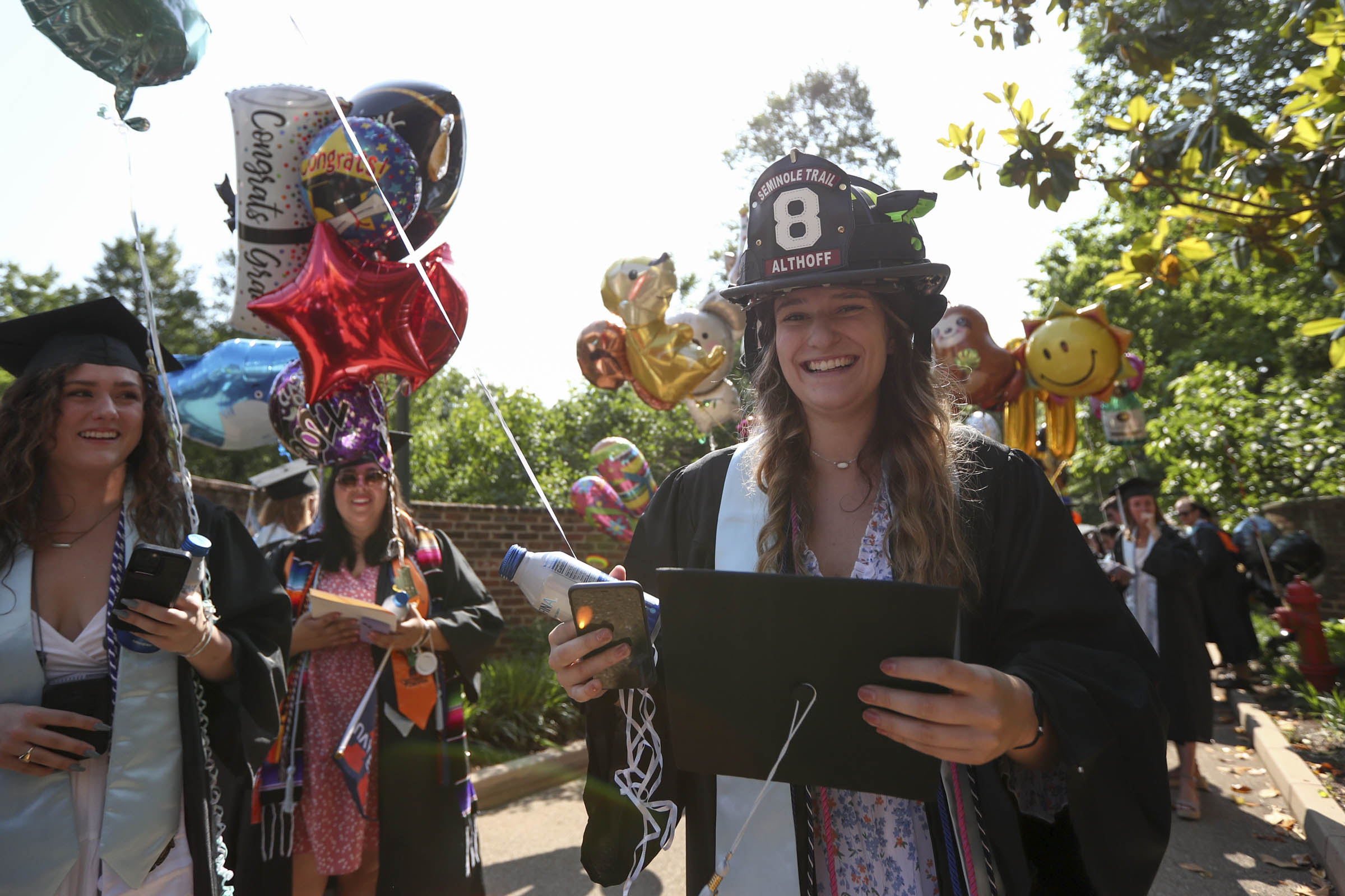 A smiling Jordan Althoff wears a firefighter helmet and holds her grad cap
