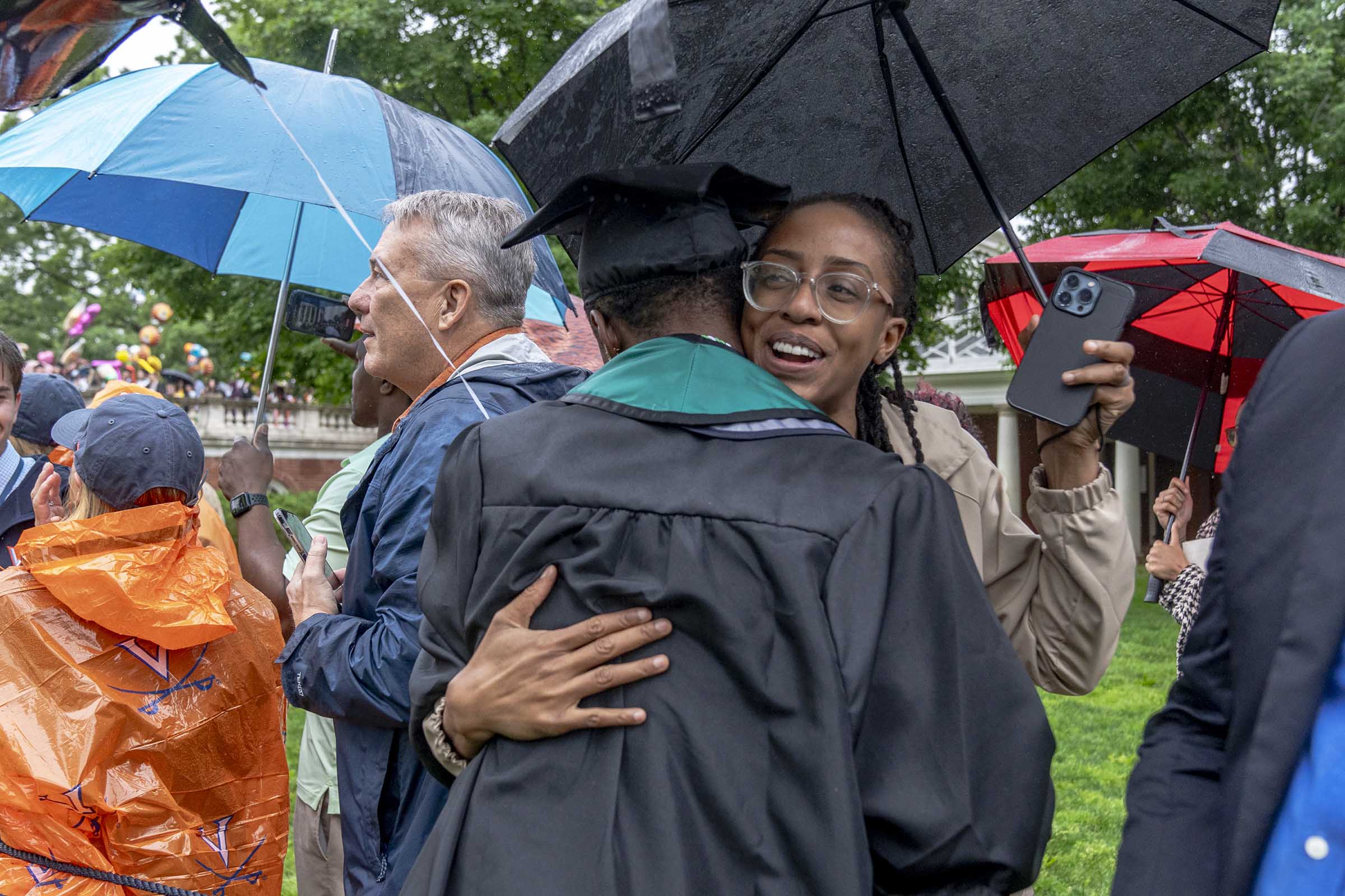 A grad and loved one embrace under an umbrella