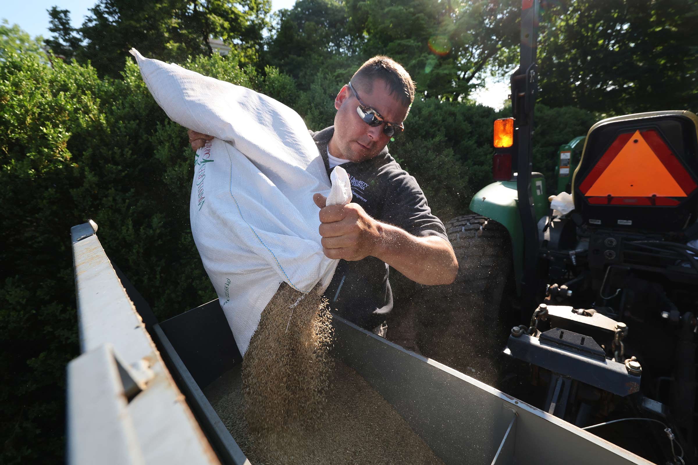 A member of the Facilities Management team pouring a large bag of grass seed into a spreader