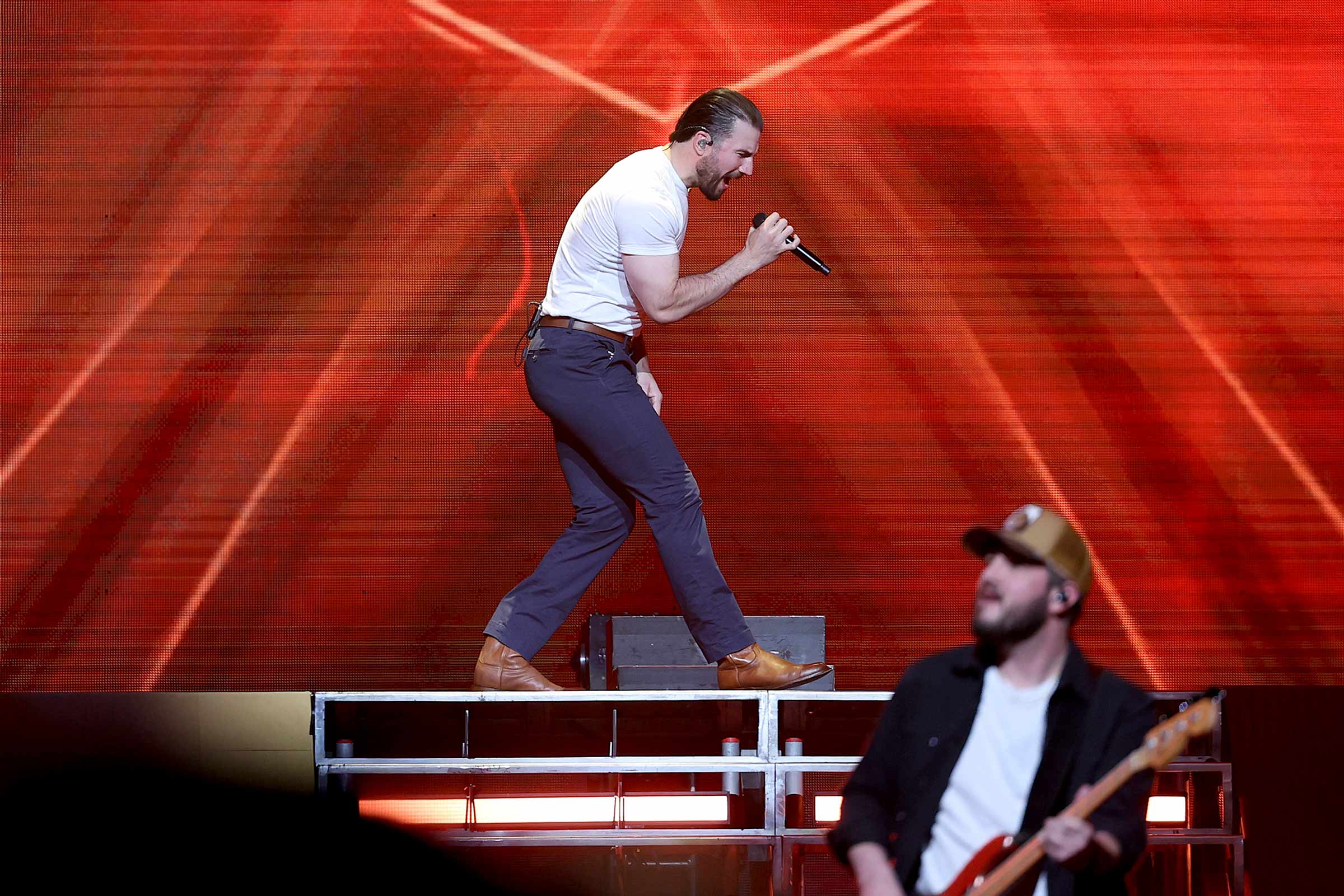 Sam Hunt singing hard into the microphone on an elevated portion of the stage