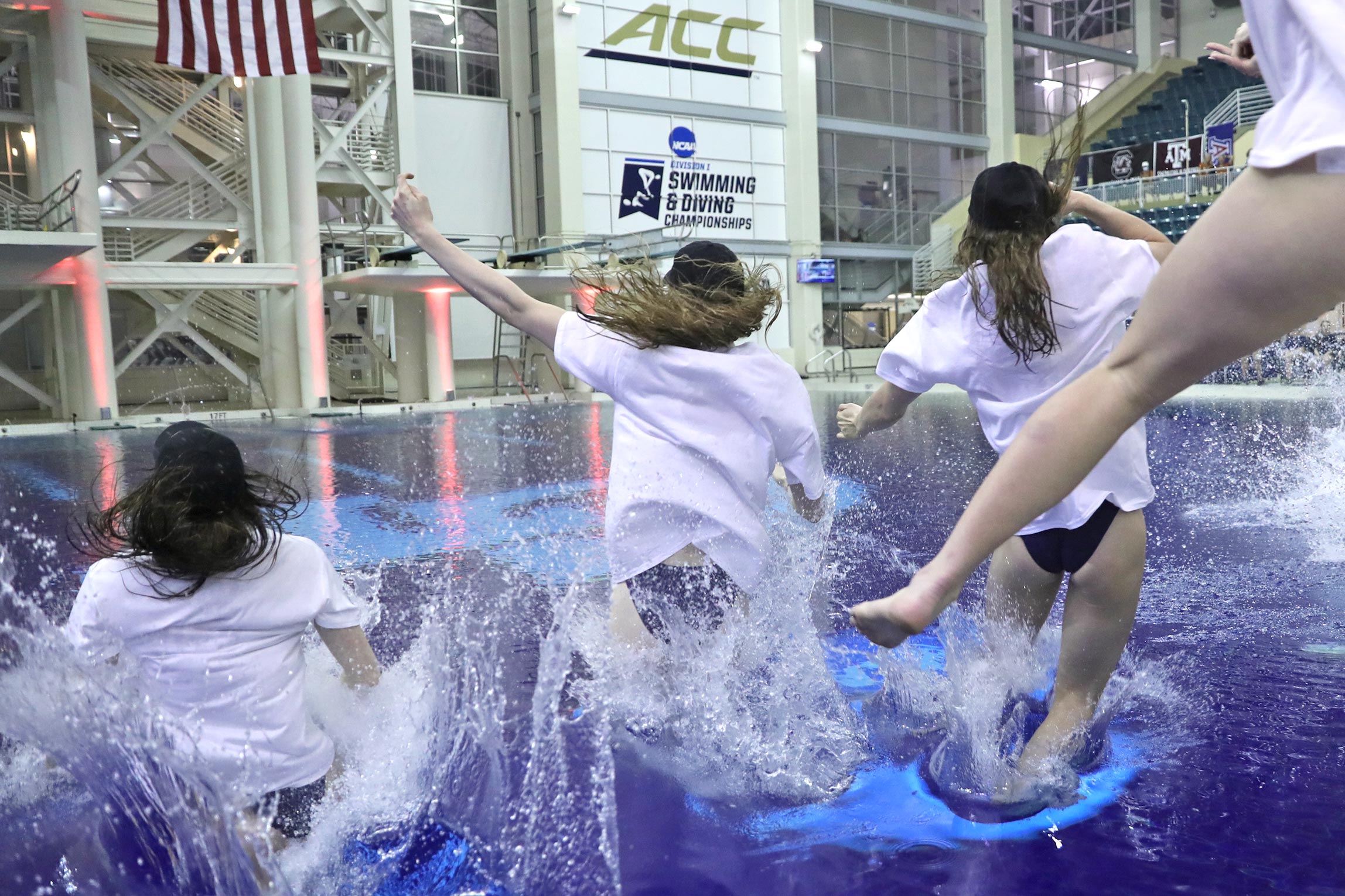 Several women in t-shirts and baseball caps excitedly jump into a pool