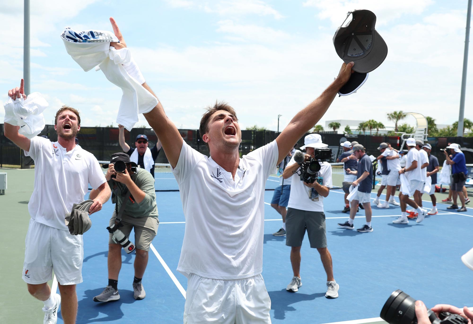Tennis player in the foreground with both hands thrown up and pointing in celebration